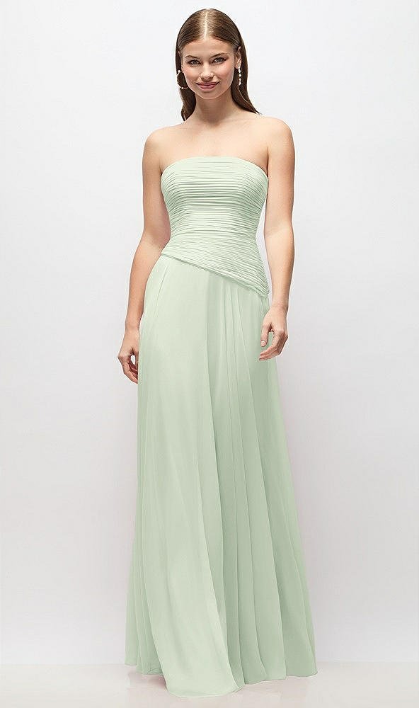 Woman in a strapless, light green pleated evening gown standing against a plain white background.