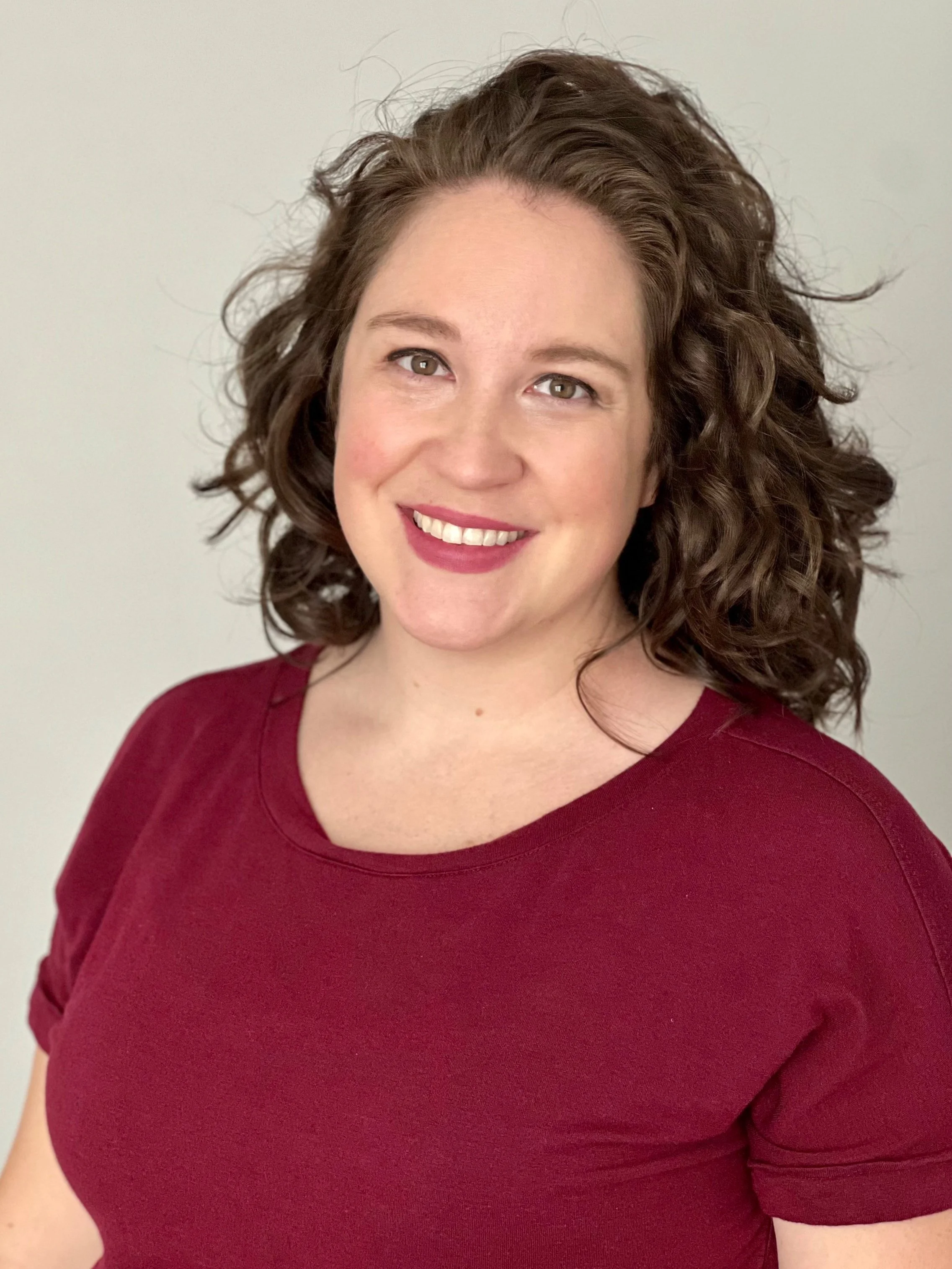 Smiling woman with curly hair wearing a maroon shirt, looking at the camera.