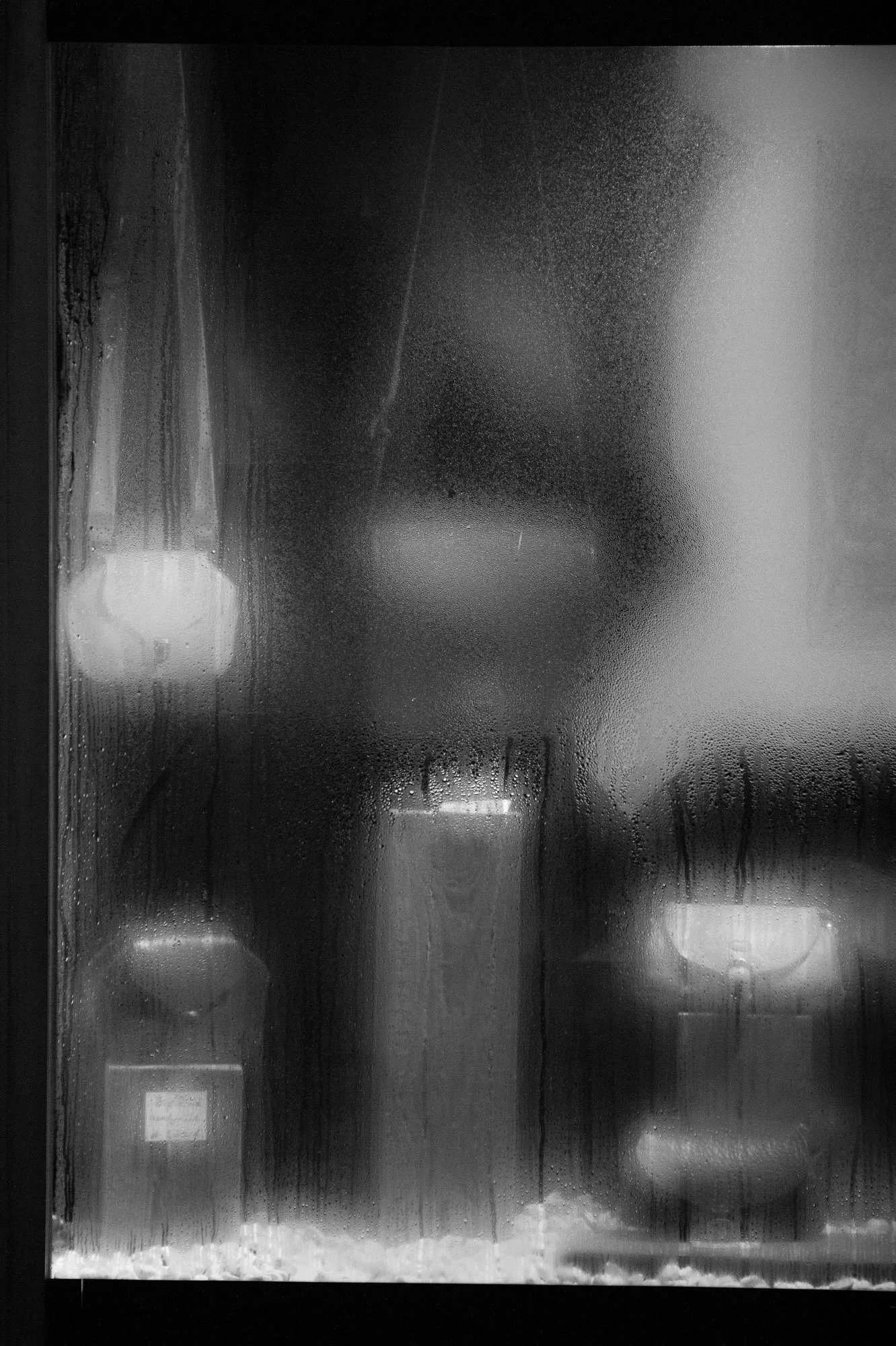 Frosted glass window with condensation, revealing blurred bottles inside a fridge or display case.