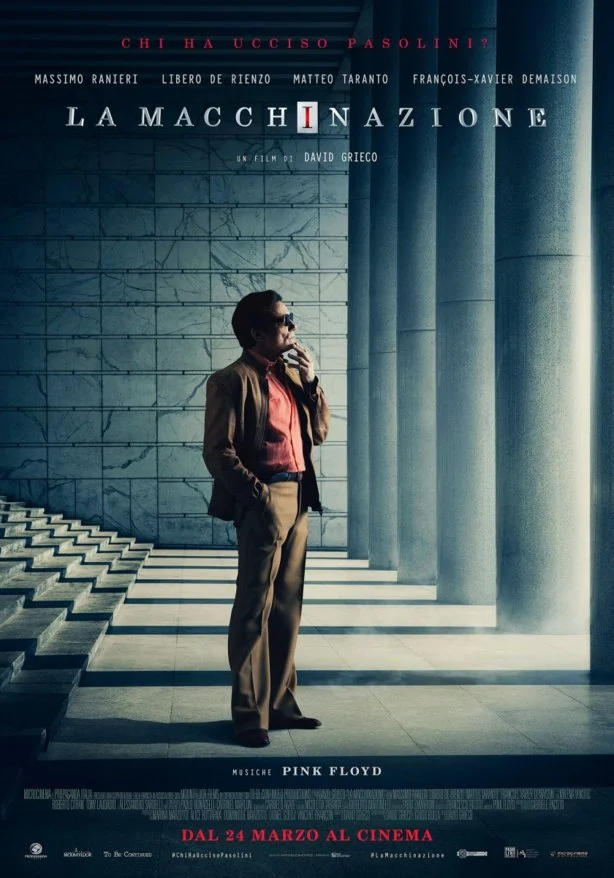 A man wearing sunglasses, a brown jacket, and beige pants standing indoors next to large marble columns and stairs, with a marble wall in the background, promoting the film 'La Macchina Nazionale' with Pink Floyd music.