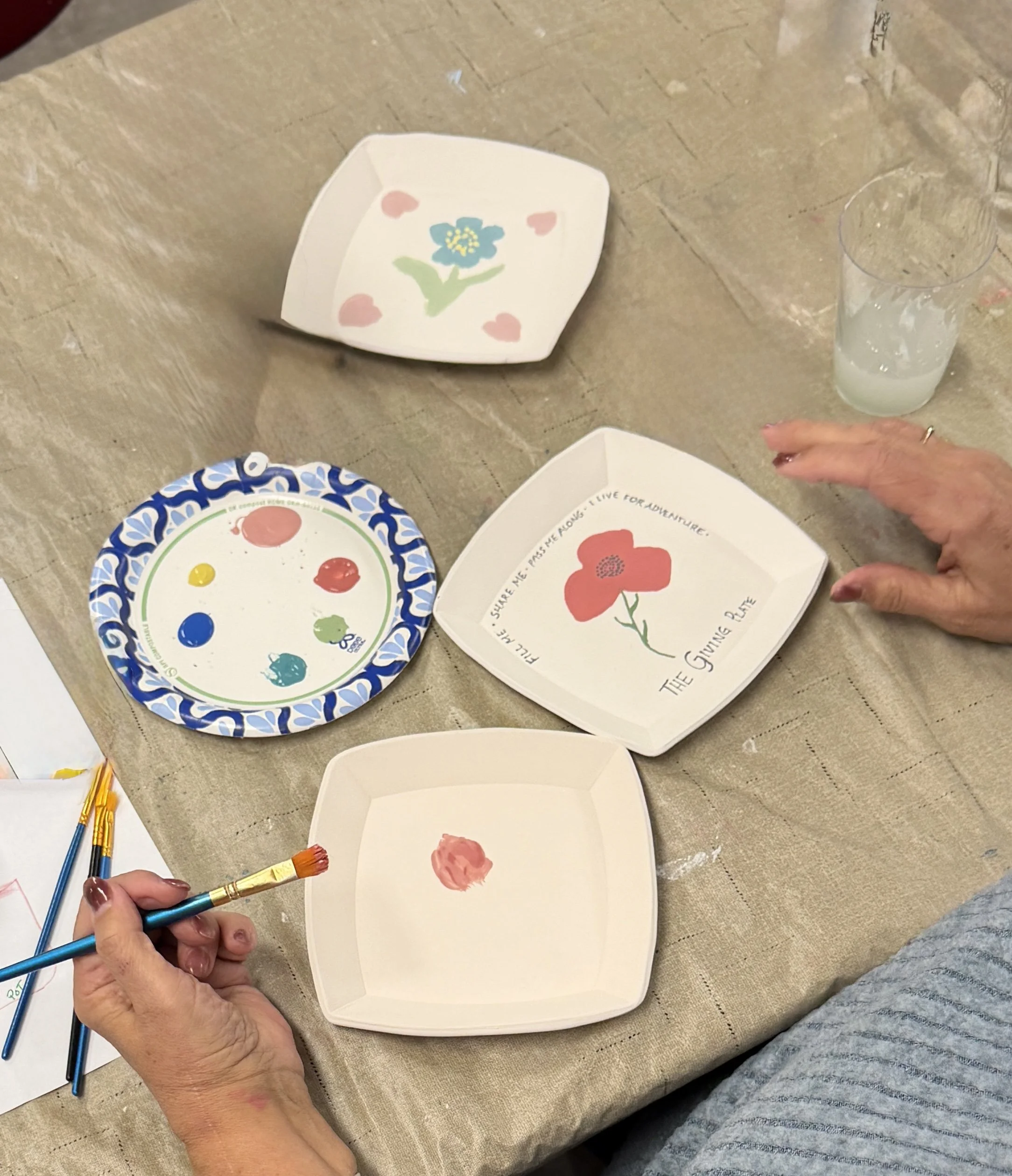 Hands painting floral designs on ceramic plates and bowls during an art activity.