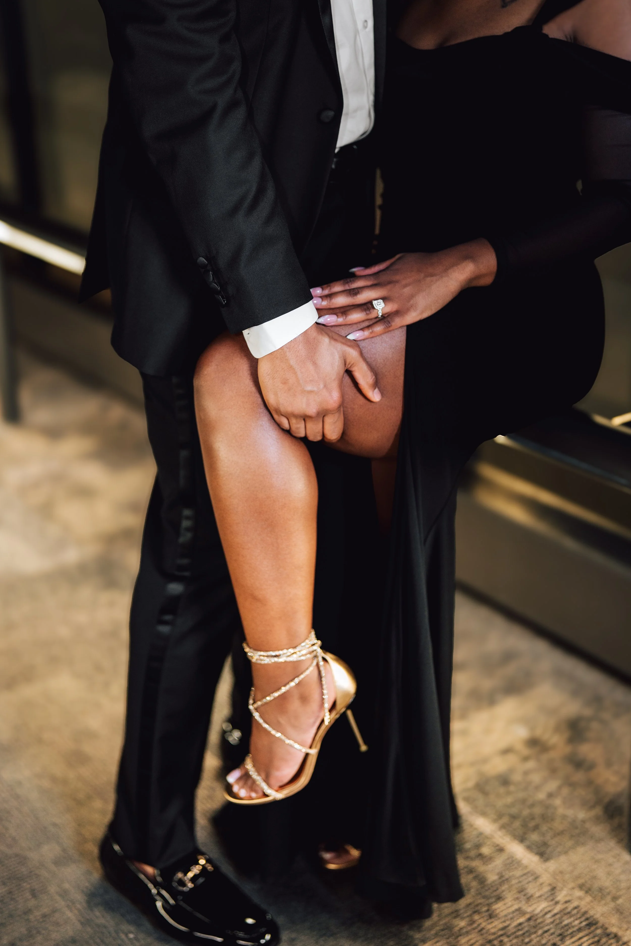 A couple in formal attire, with the man lifting the woman's leg showing her gold high heel shoes.