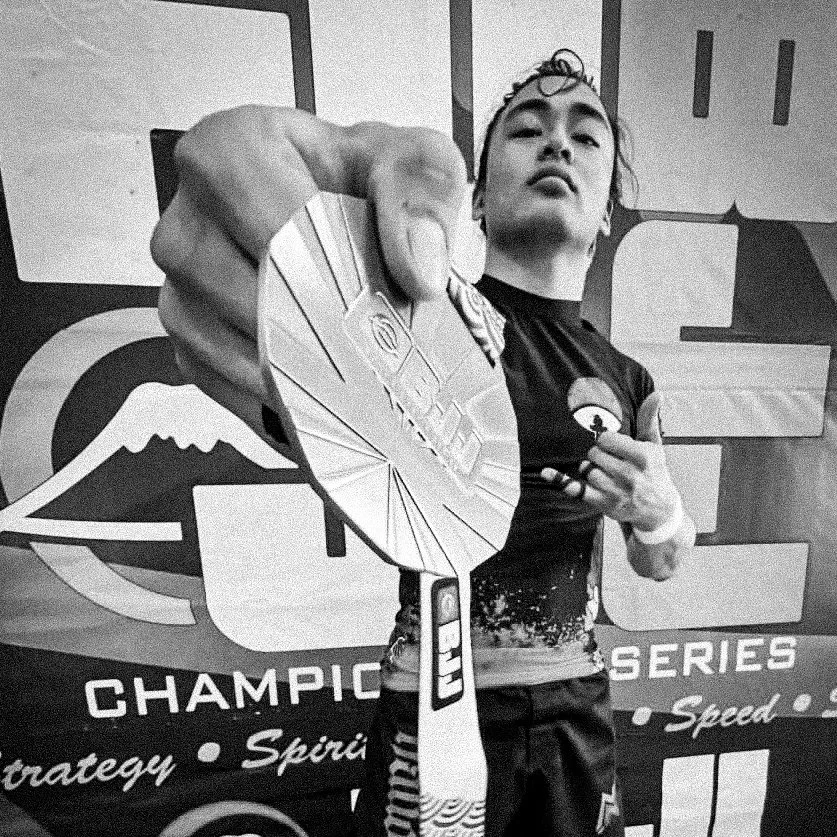 A person holds a finisher's medal from a racing event in front of a backdrop with the words 'FUJI BJJ Championship Series.'