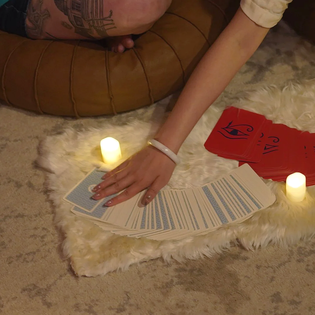 Three tarot cards on a white surface surrounded by flower petals and a pink candle. The cards read: 'The Age of Light,' 'Dance with Life,' and 'Starseed.'