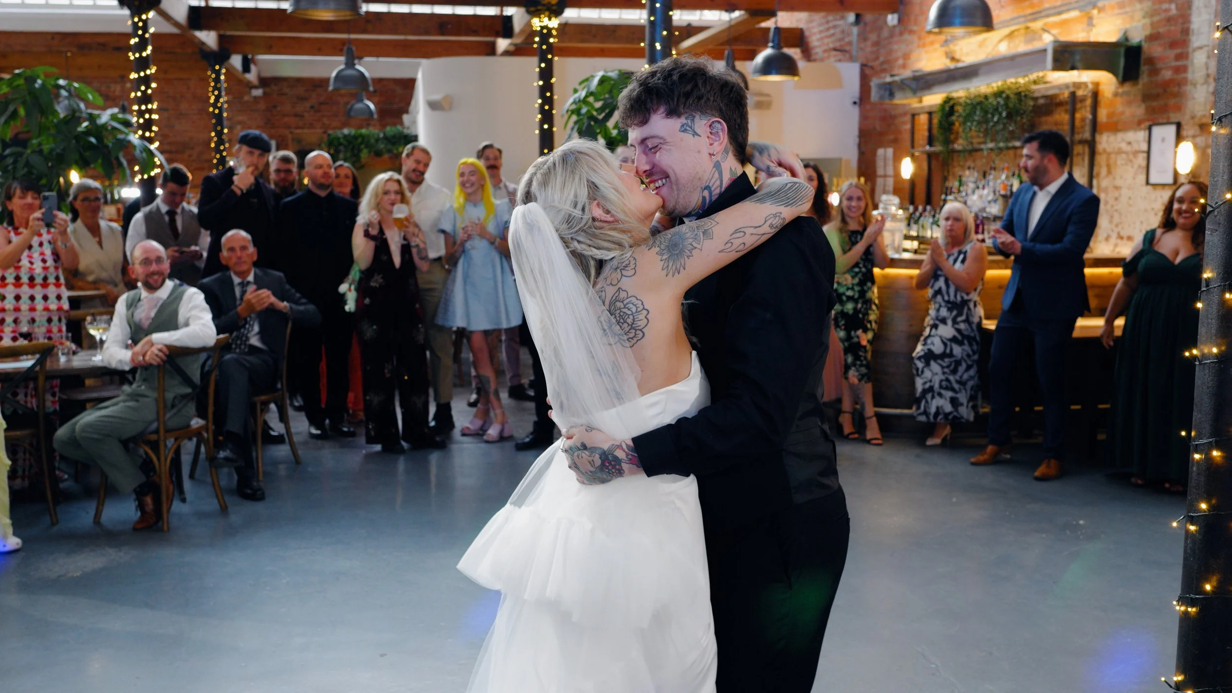 K+M, alternative newlyweds with tattoos celebrate their wedding with a first dance at the industrial wedding venue the River Mill in Derby, surounded by their families and friends. Taken by Derbyshire wedding videographer Laura Baker Productions.