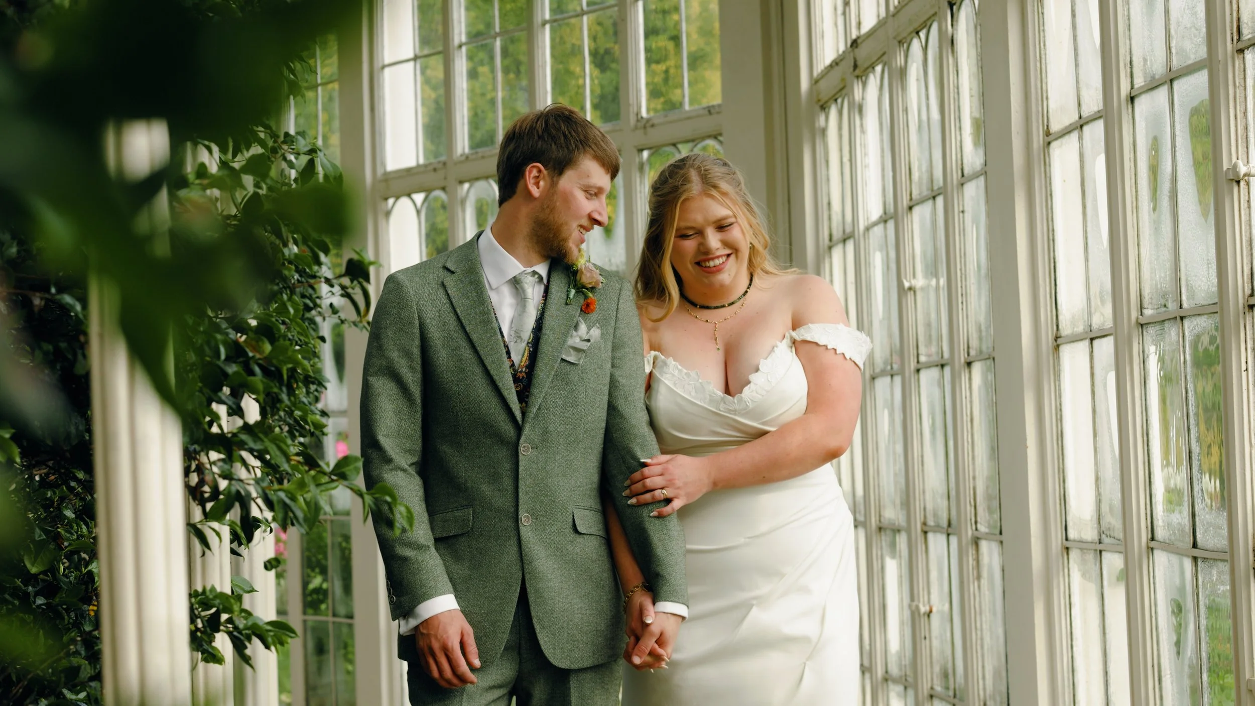A bride and groom walk hand in hand during their wedding reception inside Camellia House at Wollaton Hall wedding venue in Nottingham, a still from Nottingham wedding videographer Laura Baker Productions