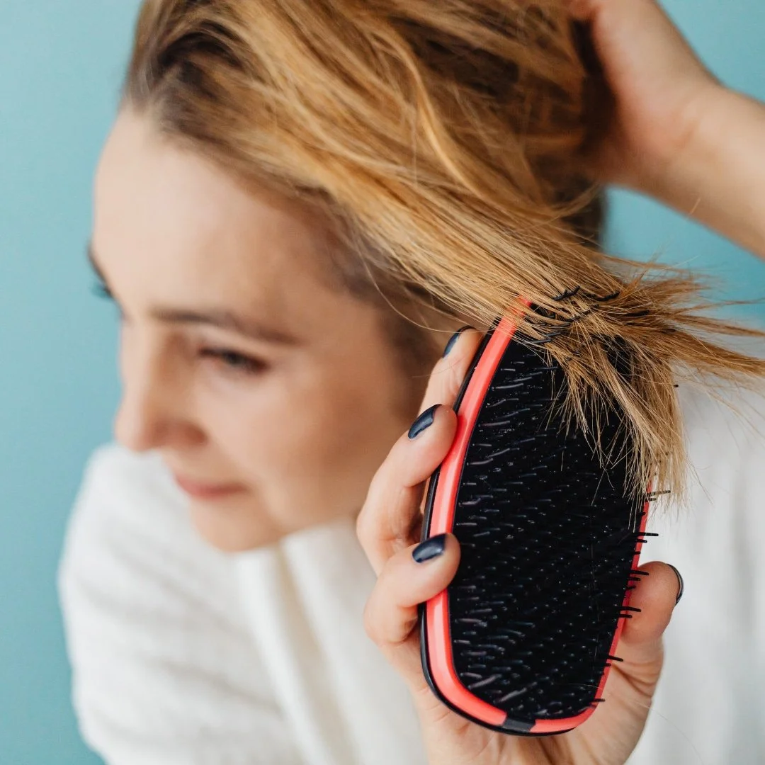 This is an image of a woman with healthy blonde hair brushing her hair with a pink hand brush