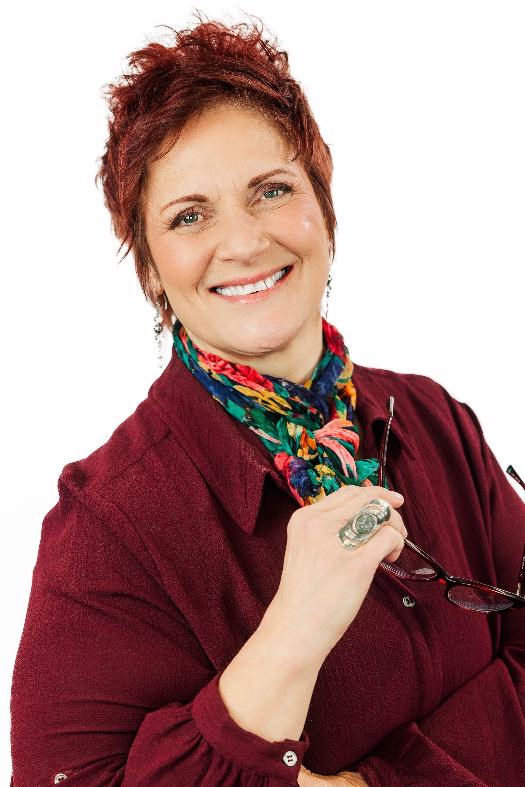 Woman with short auburn hair and hoop earrings smiling in a colorful dress.