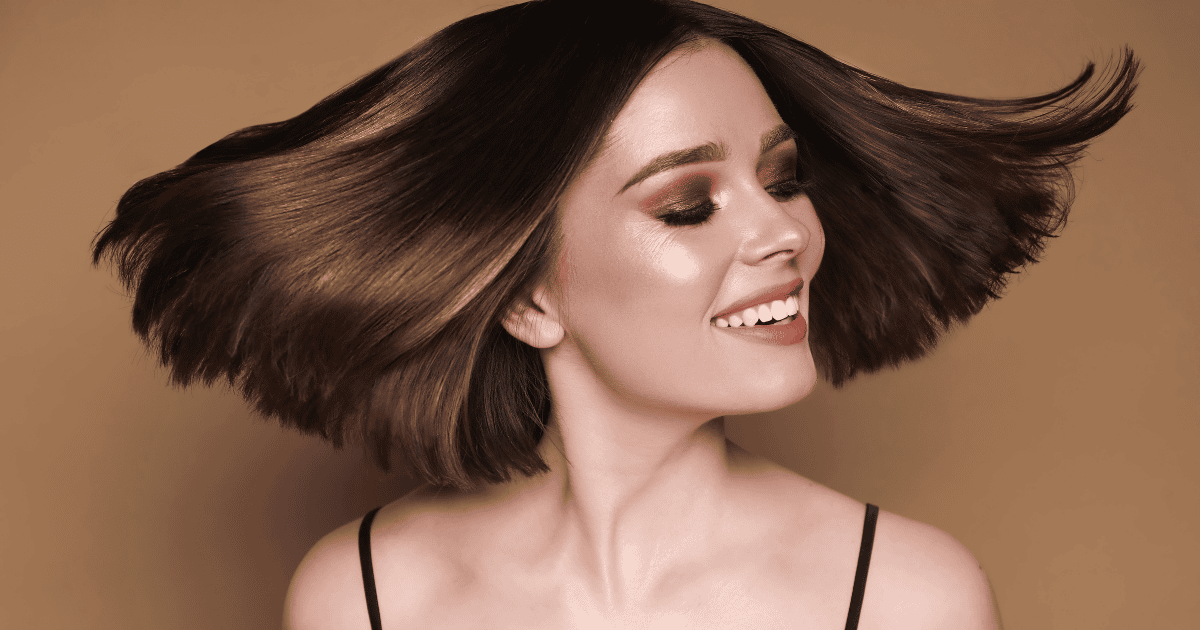 This is an image of a brunette woman flipping her hair. She has nice neutral makeup with super shiny hair