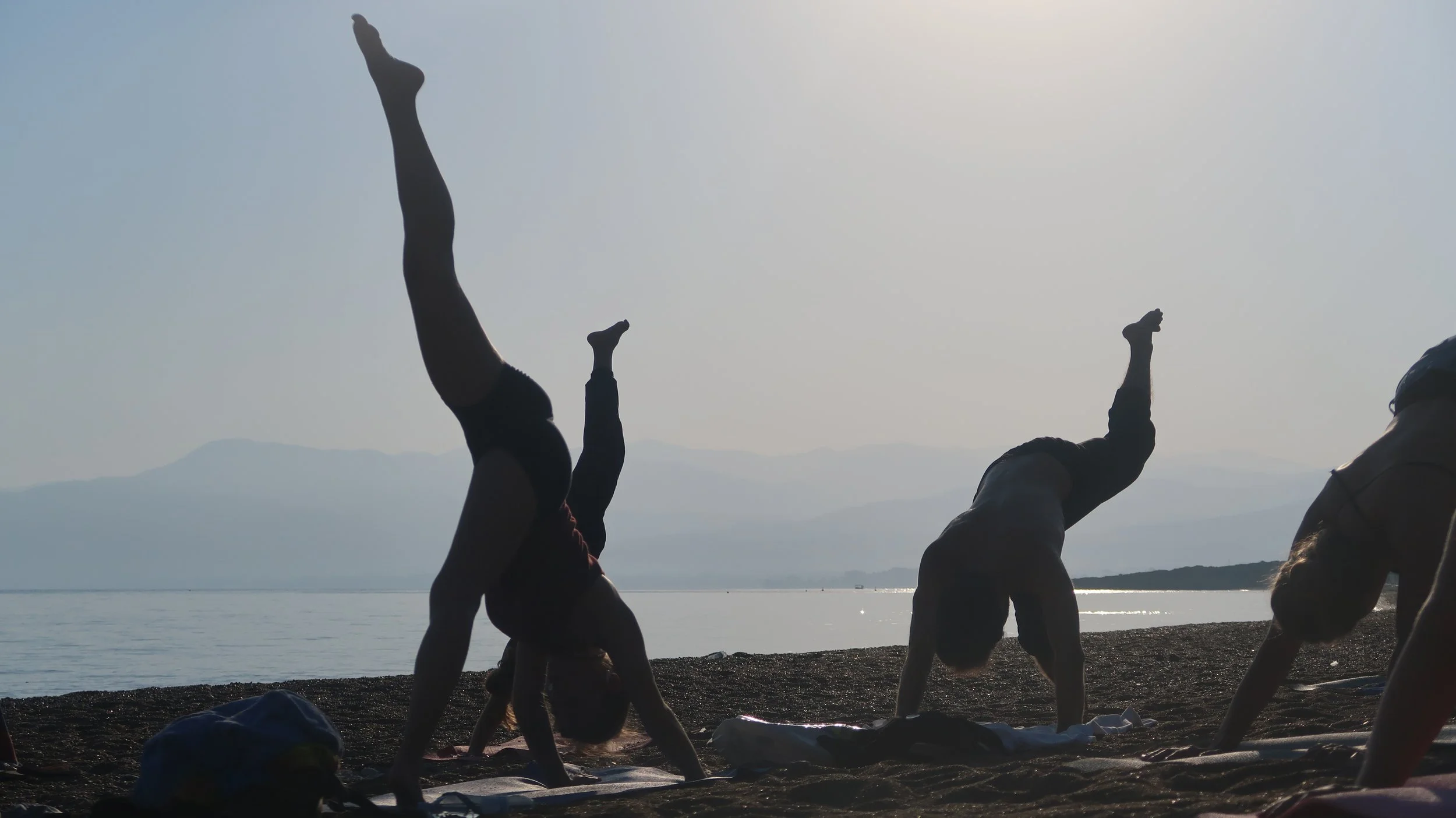 People practicing yoga on the beach during sunset, silhouetted against the sky and water