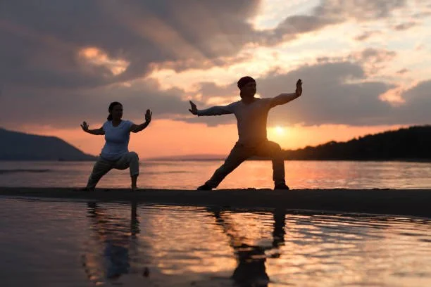 Two people practicing yoga on the beach at sunset.