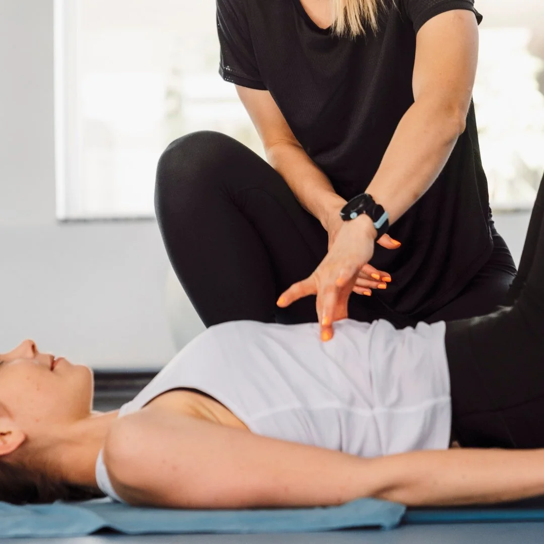 A woman lying on a blue exercise mat during physical therapy, with a therapist assisting her by applying pressure to her knee.