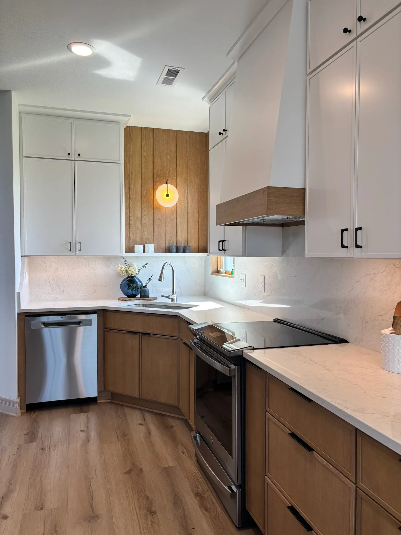 Modern kitchen with white upper cabinets, wood lower cabinets, white countertops, stainless steel appliances, and a decorative vase with flowers.