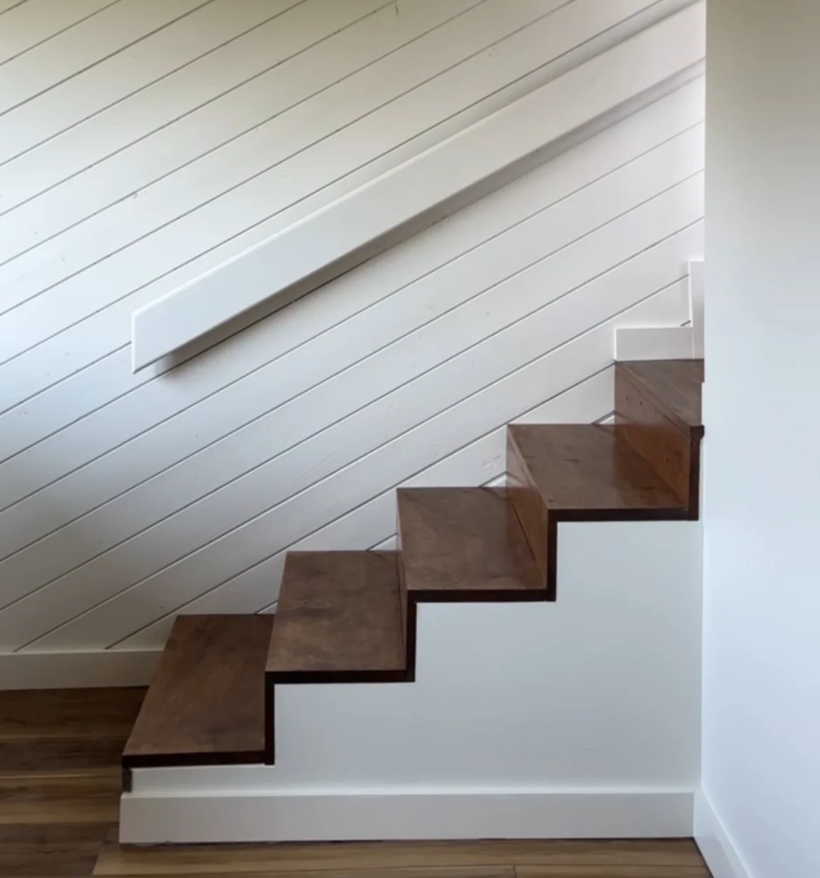 A staircase with wooden steps ascending along a white wall with horizontal shiplap paneling.