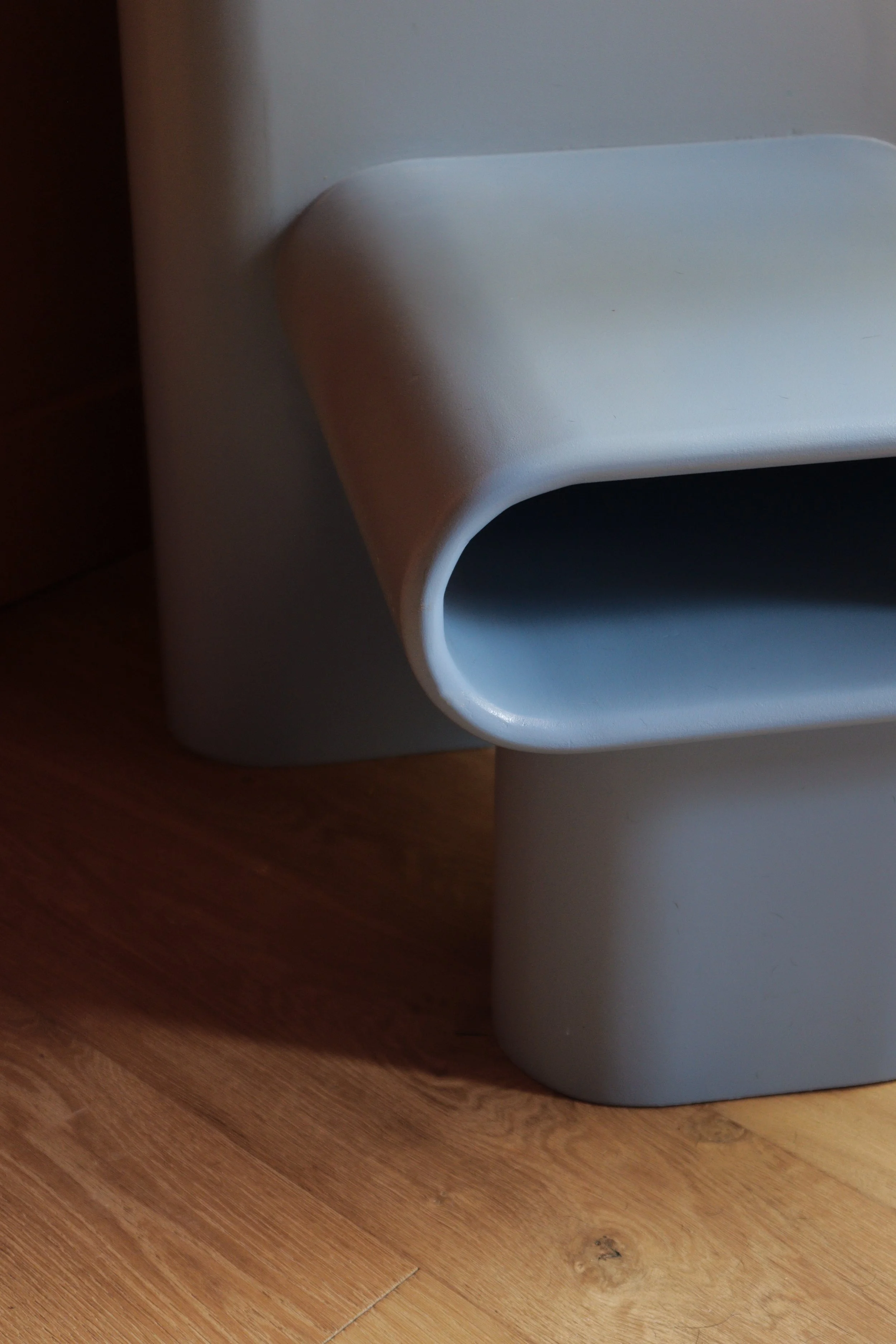 A close-up view of a sculptural chair with curved edges and smooth light blue paint