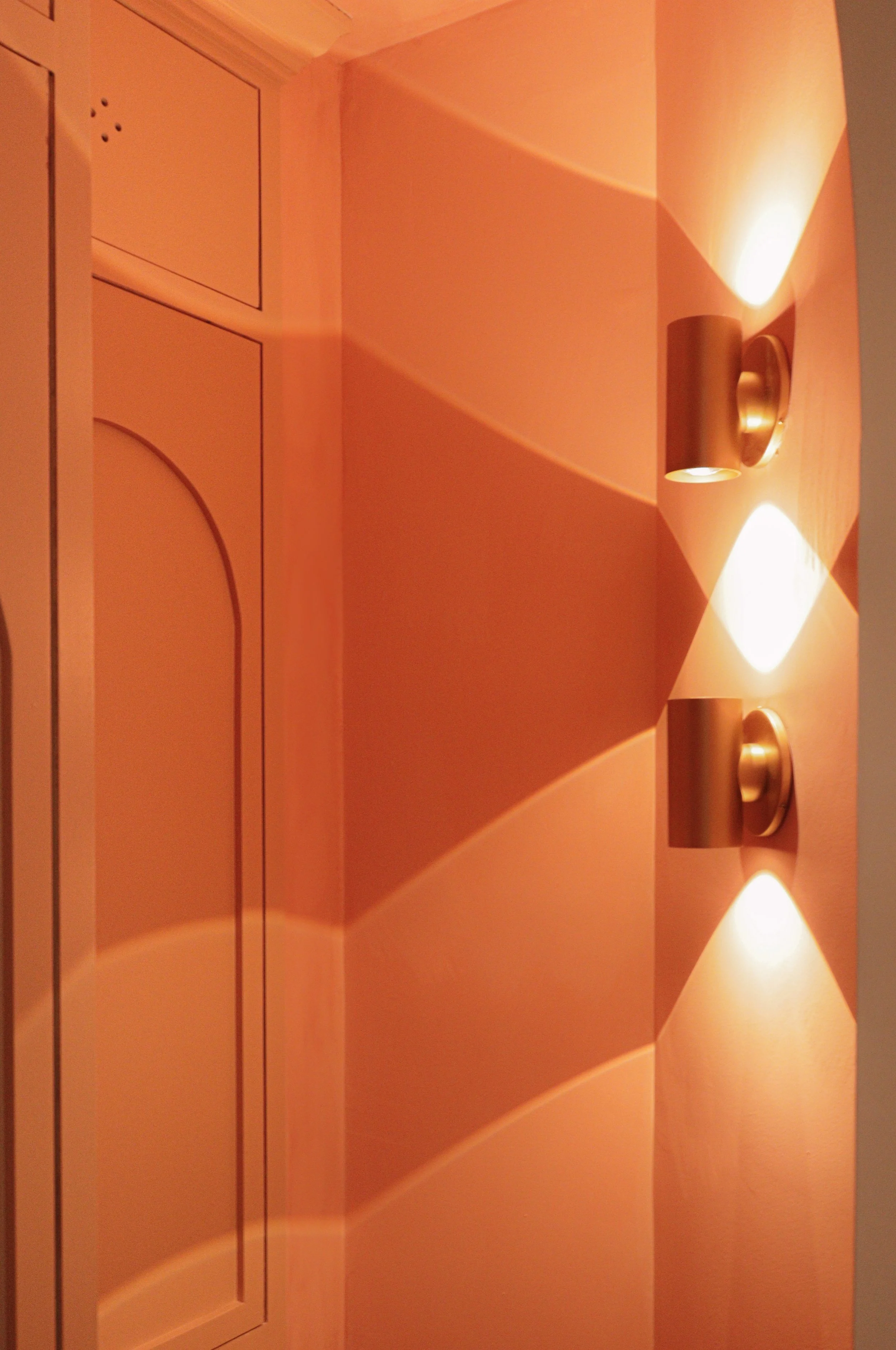 A wall with three installed light fixtures casting light and shadows on the orange-colored wall and ceiling.