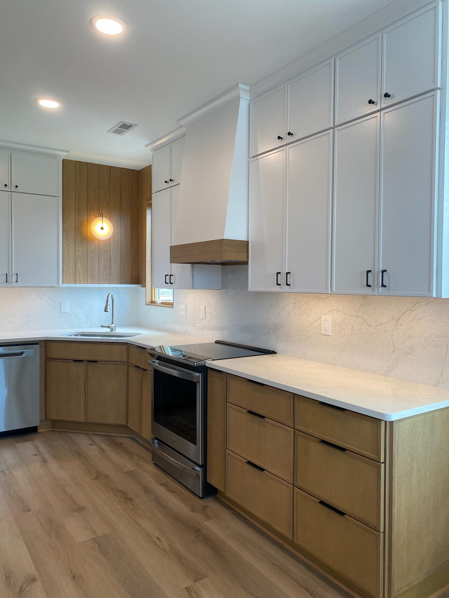 Modern kitchen remodel in Manteo with white oak and white slim shaker cabinetry, white quartz countertop and backsplash and custom white kitchen hood with oak band
