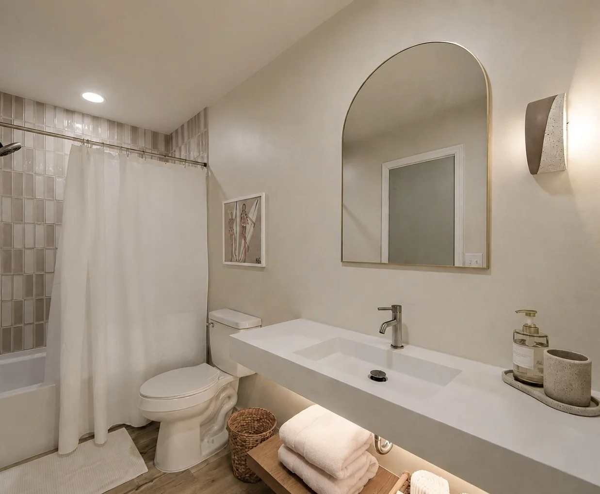Modern bathroom with a shower area, a toilet, a large mirror, a white countertop sink with a faucet, and decorative accessories on the sink counter.