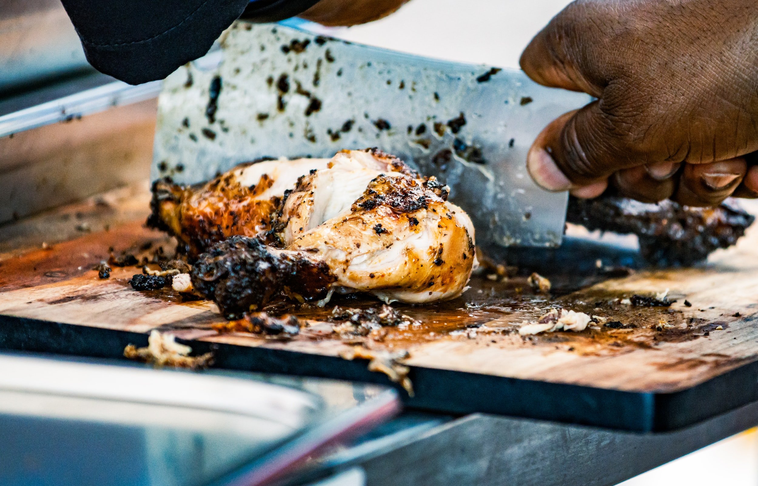 Person slicing roasted chicken on cutting board with cleaver