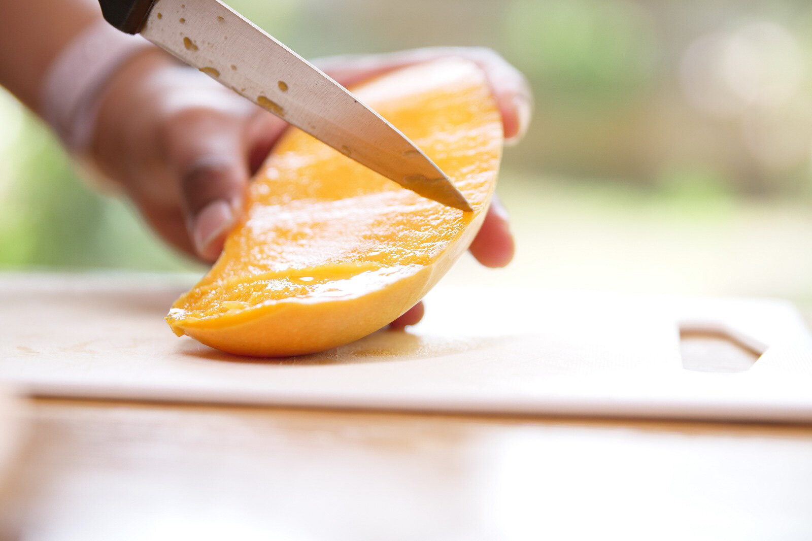 Person slicing a ripe mango with a knife on a cutting board.