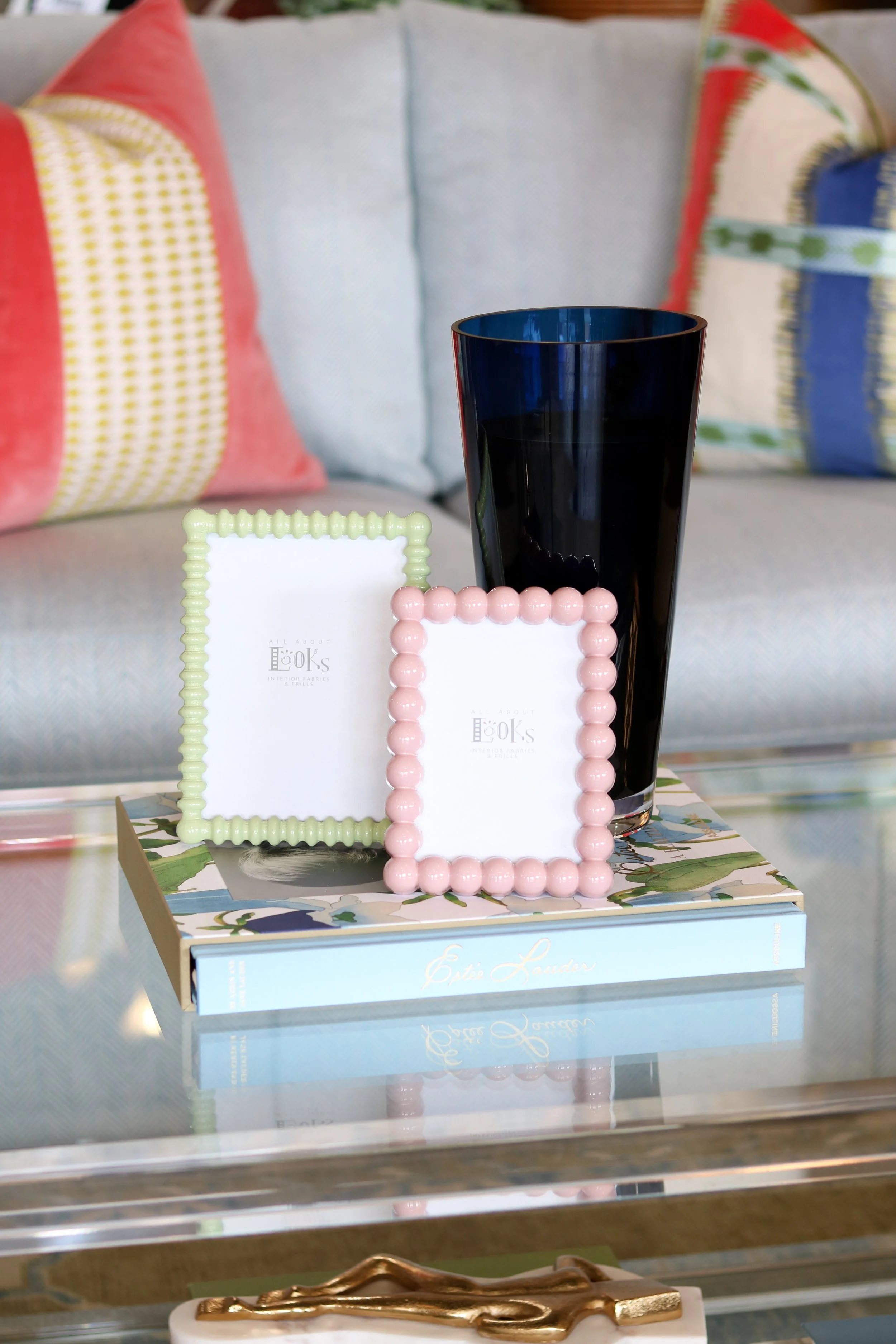 Decorative display on a table with picture frames, a black glass, and a colorful box in the background.