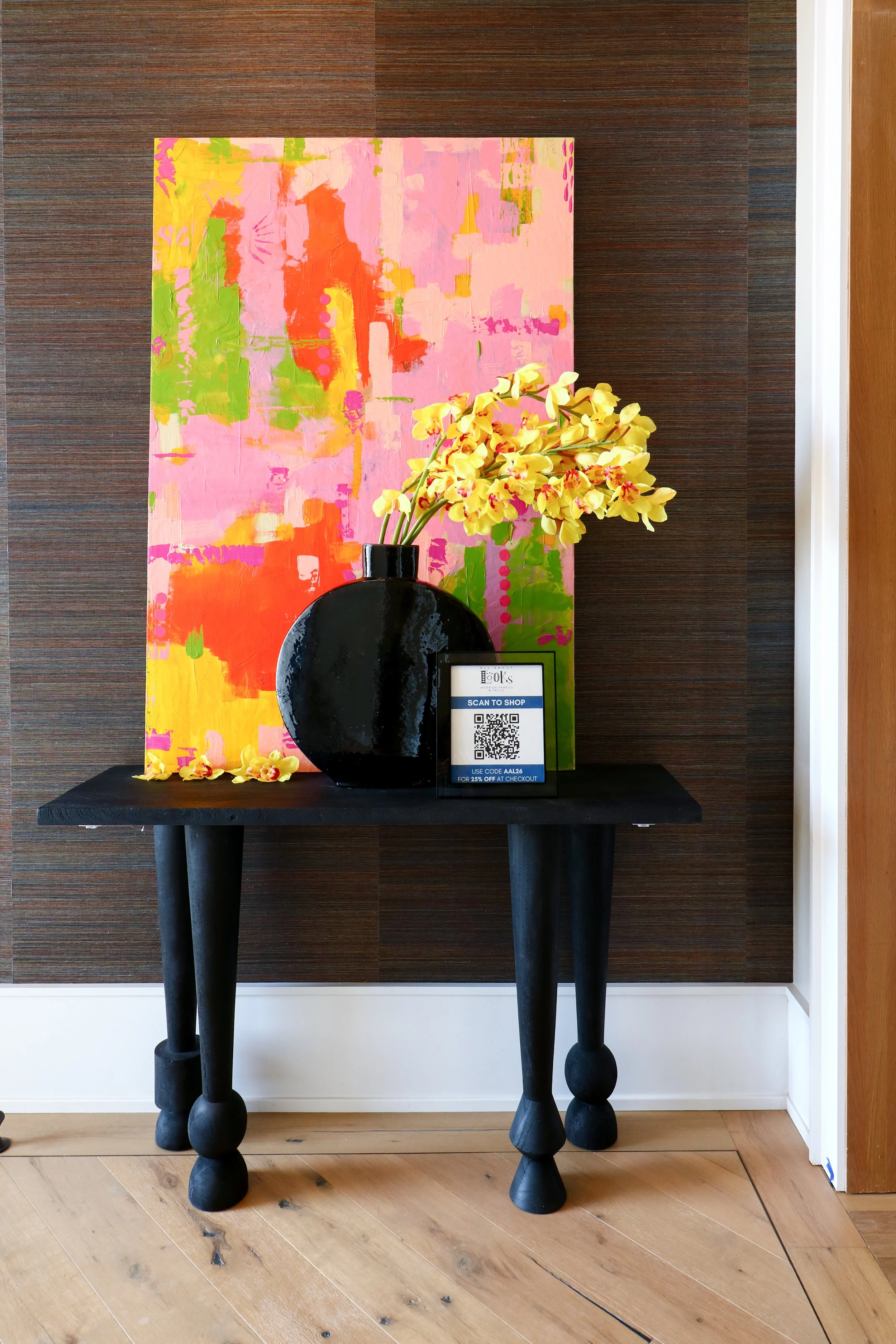 Black table with a black vase of yellow orchids and a colorful abstract painting in the background.