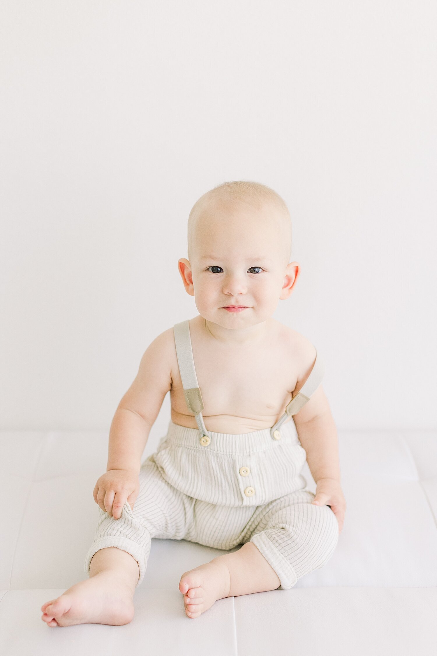 One year old sitting up, wearing suspenders for his first birthday photoshoot with Ambre Williams Photography.