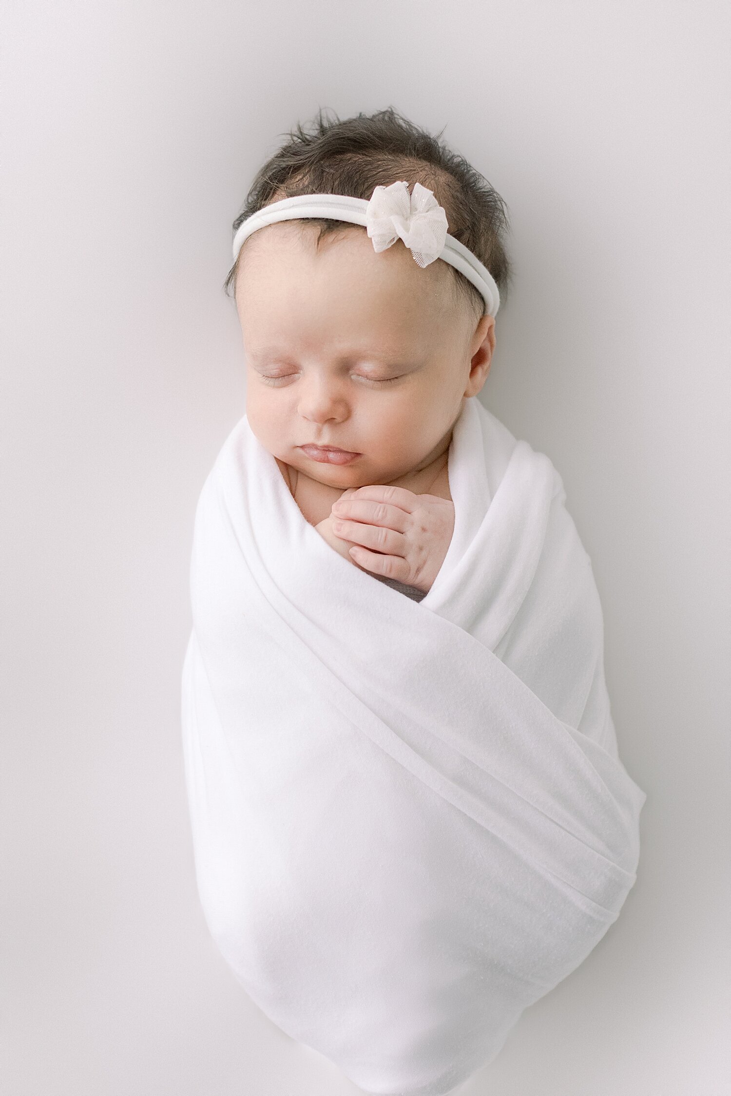 Baby girl swaddled in white with a white headband. Photo by Ambre Williams Photography.