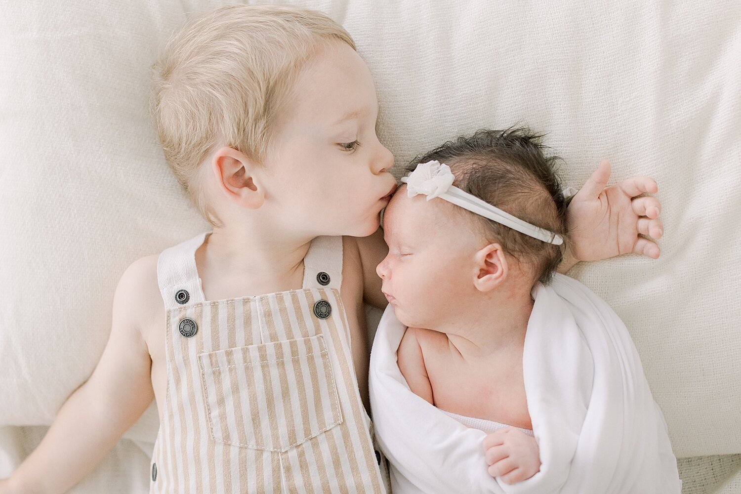 Big brother giving his baby sister a kiss on her forehead during her newborn photoshoot in Newport Beach with Ambre Williams Photography.