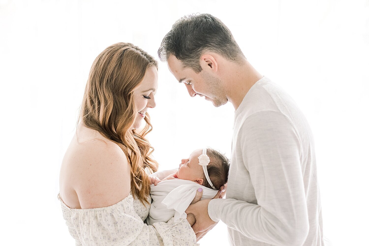Backlit photo of Mom and Dad holding their daughter. Photo by Ambre Williams Photography.