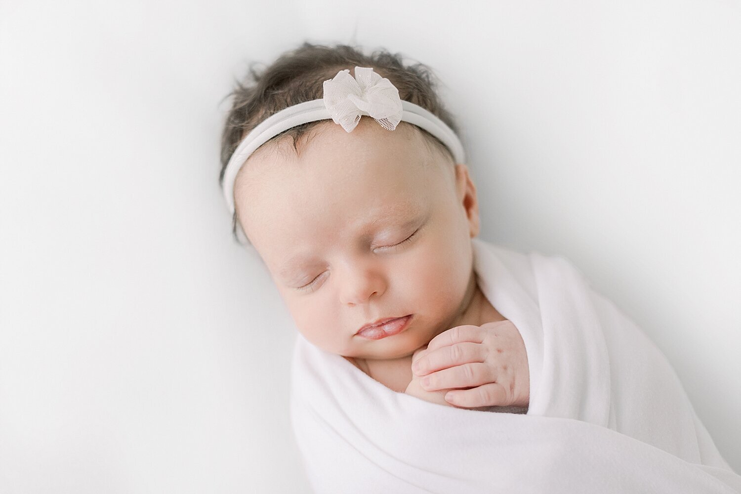 Newborn baby girl swaddled with her hands folded on her chest. Photo by Newport Beach Photographer, Ambre Williams Photography.