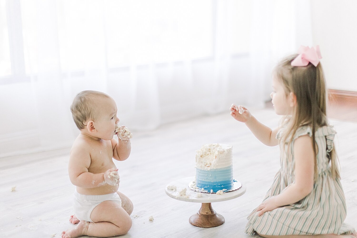 One year old boy and his big sister playing in cake smash to celebrate his birthday. Photo by Ambre Williams Photography.