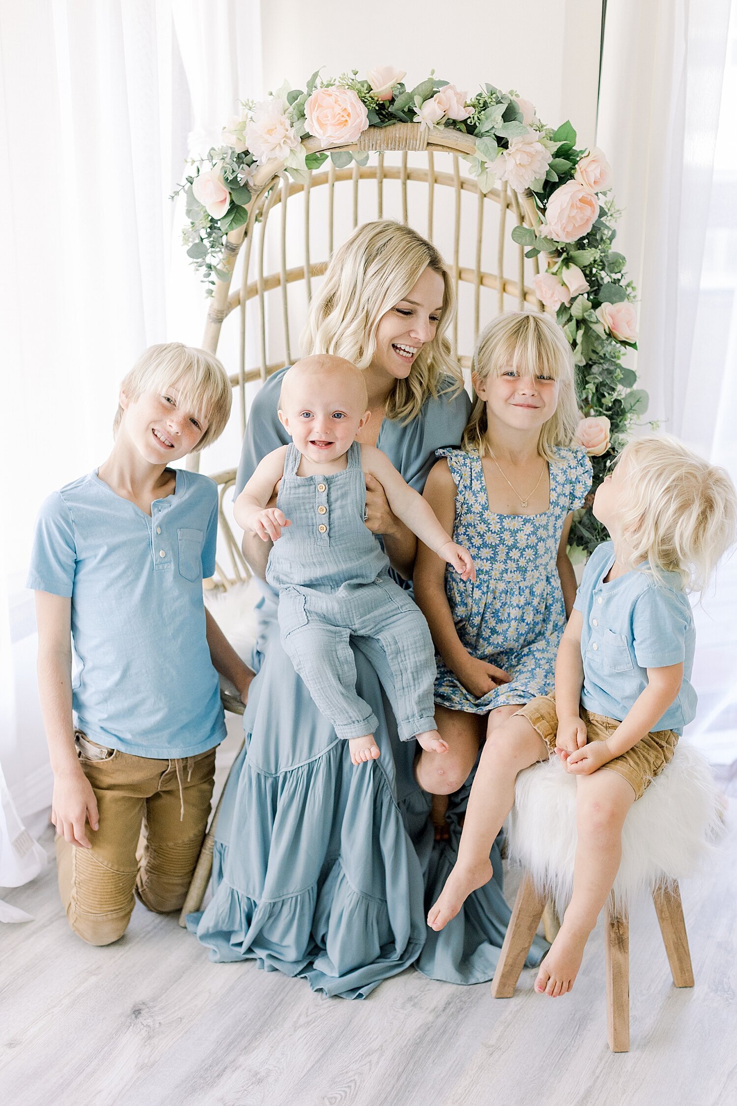 Mom sitting in a rattan chair with her four children surrounding her. Photo by Ambre Williams Photography.