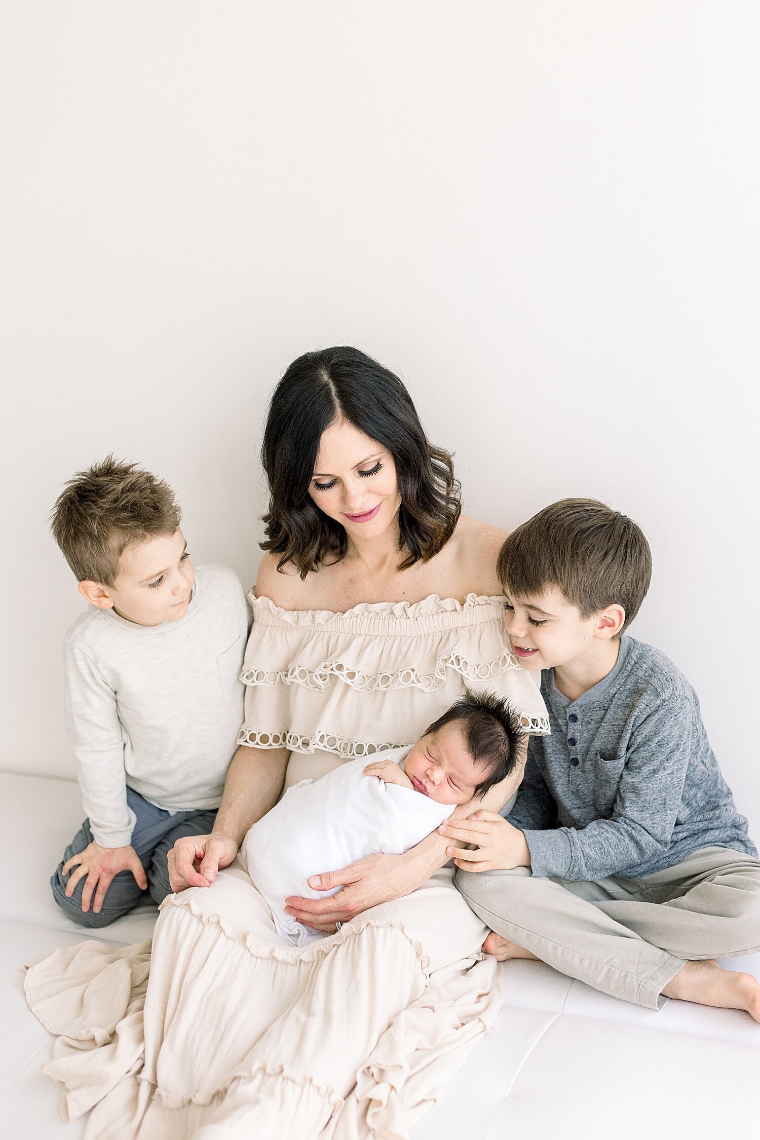 Mom and her three boys sitting on bed during newborn session for youngest baby boy. Photo by Ambre Williams Photography.