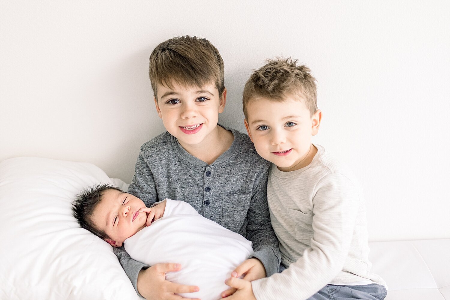 Two big brothers hold their newborn baby brother during photoshoot with Newport Beach Newborn Photographer, Ambre Williams Photography.