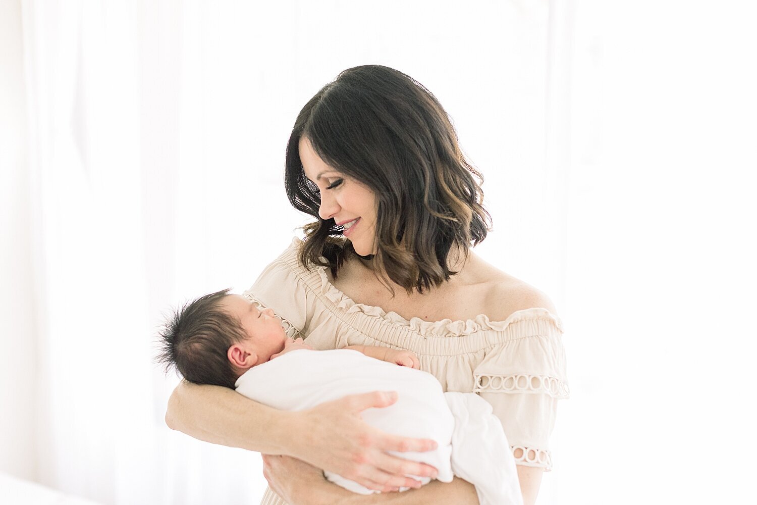 Mom holding baby boy swaddled in a white blanket. Photo by Orange County Newborn Photographer, Ambre Williams Photography.