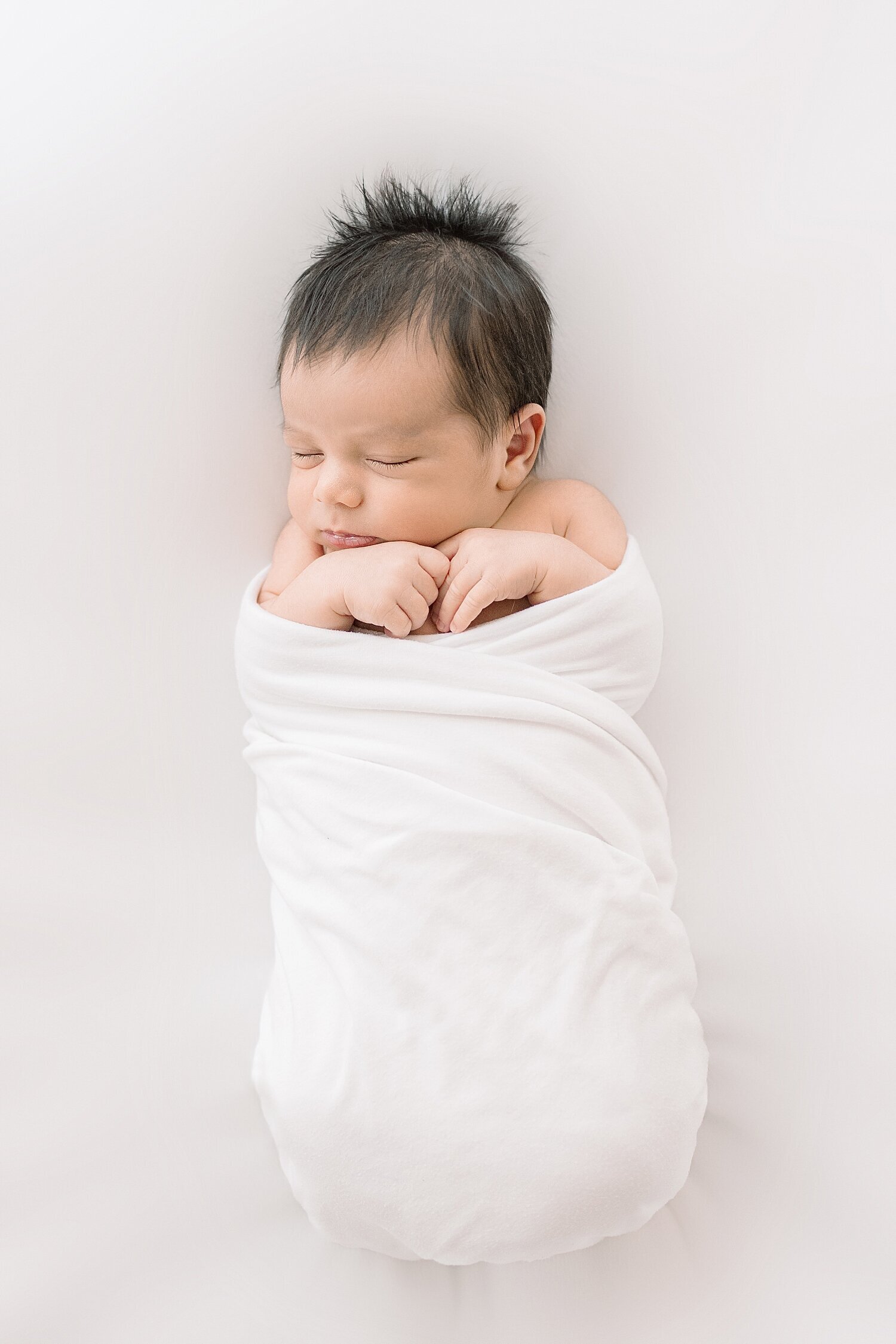 Newborn baby boy swaddled in a white blanket. Photo by Ambre Williams Photography, a newborn photographer in Newport Beach.