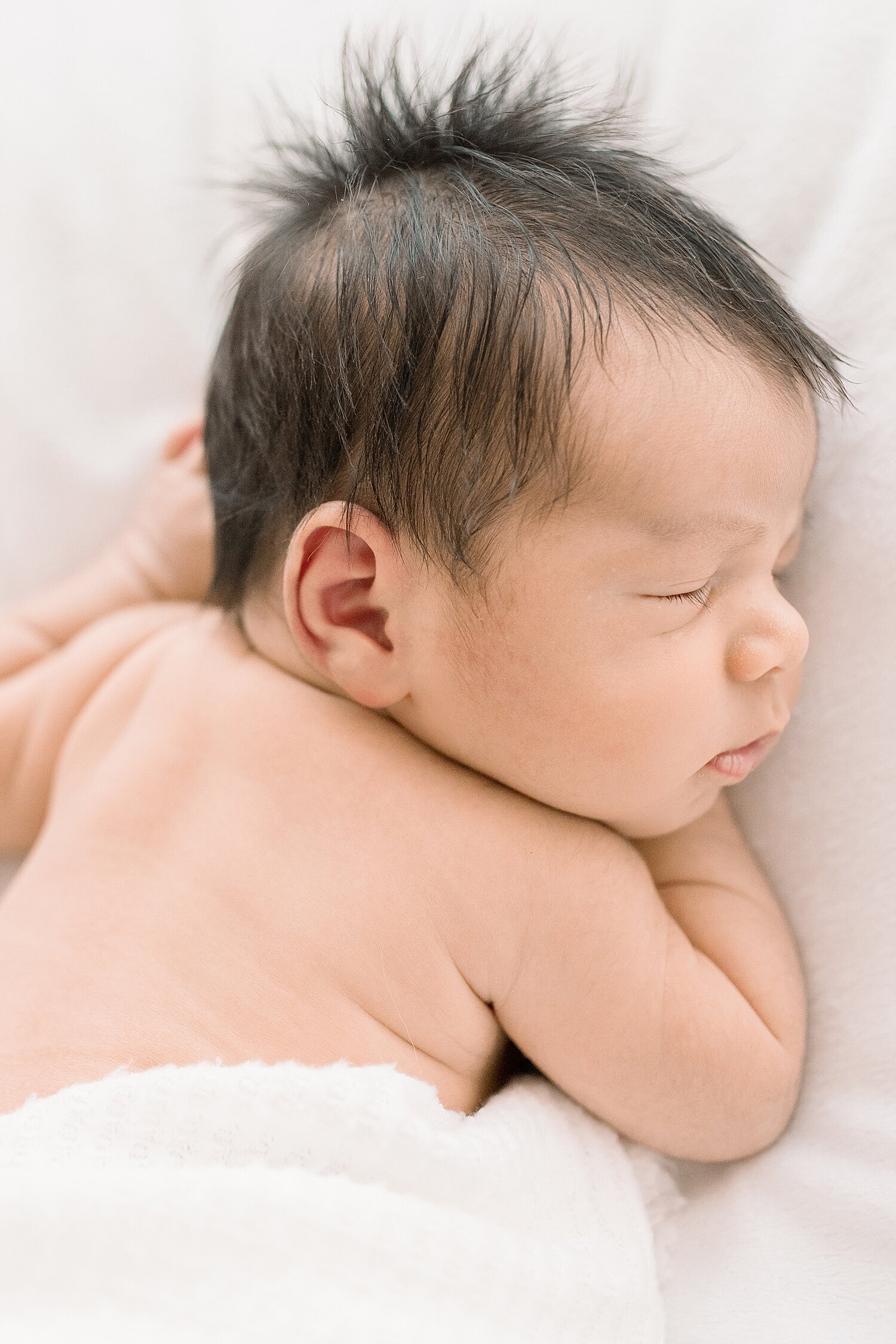 Newborn photo of baby boy with dark brown hair. He's swaddled on a white blanket. Photo by Newport Beach Newborn Photographer, Ambre Williams Photography.