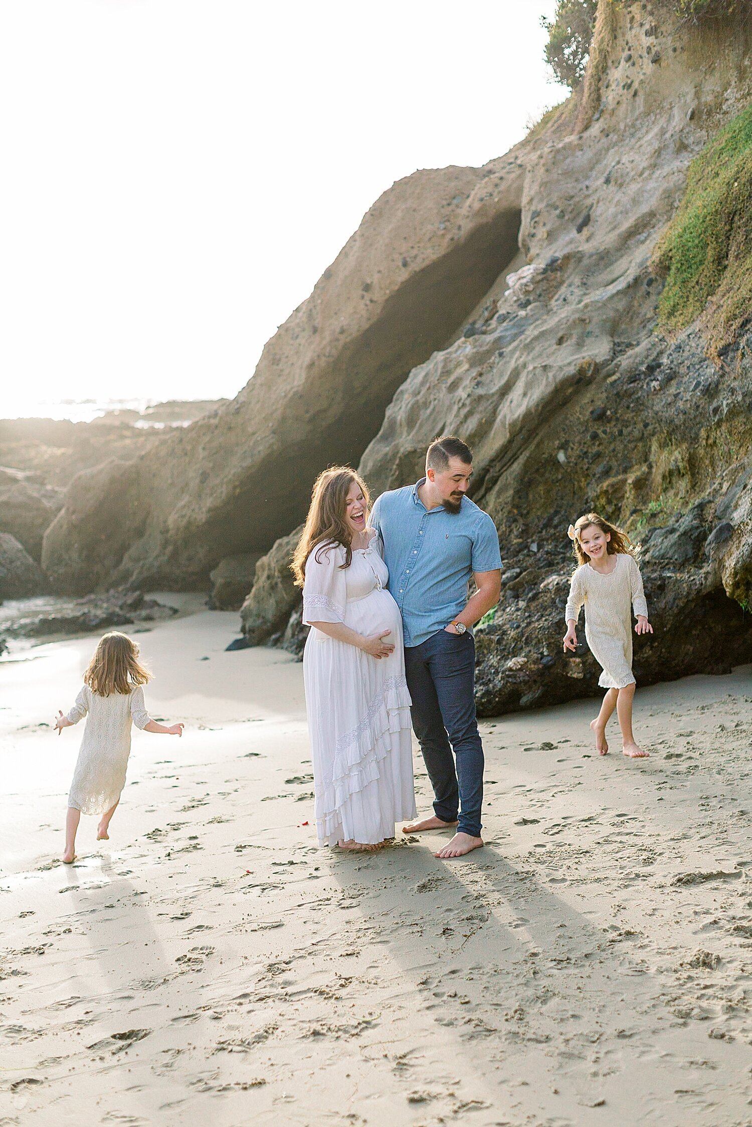 Two girls running around Mom and Dad during maternity session in Newport Beach at Corona del Mar. Photos by Ambre Williams Photography.