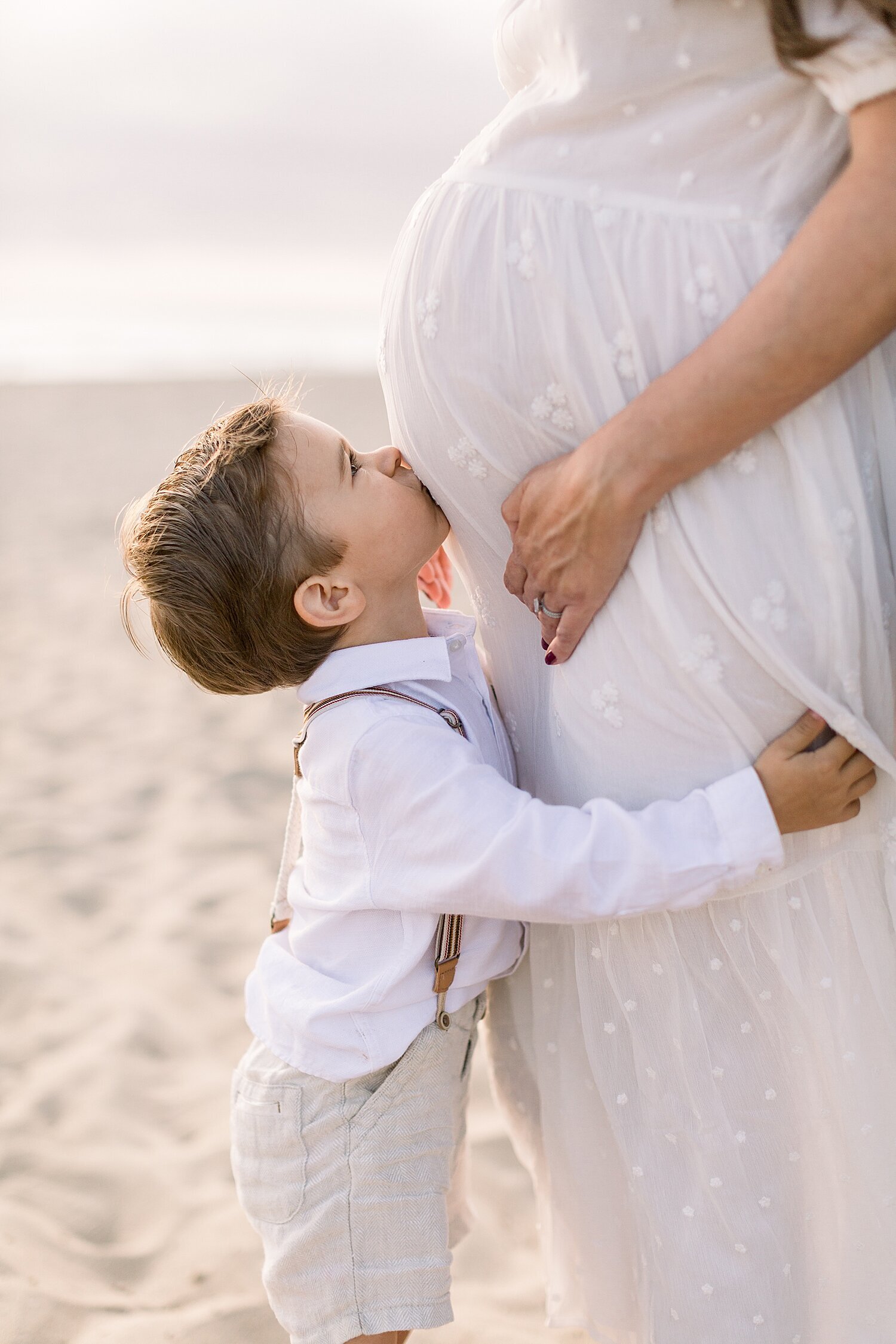 Big brother kissing Mama's belly during maternity session on the beach with Ambre Williams Photography.
