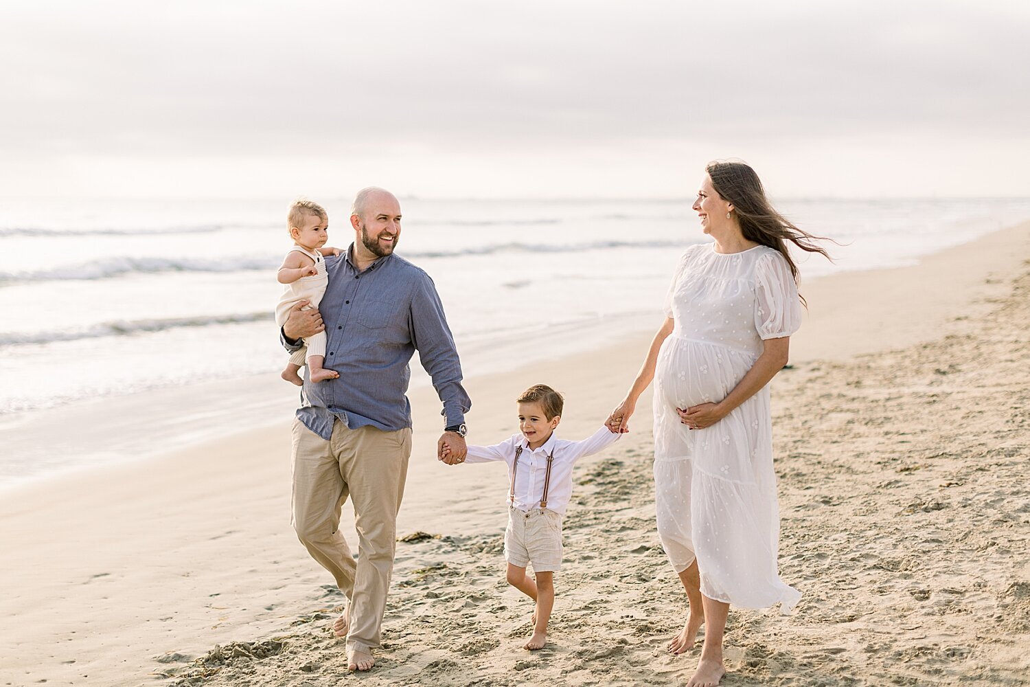 Family walking along the water at Huntington Beach during sunset maternity session. Photos by Ambre Williams Photography.