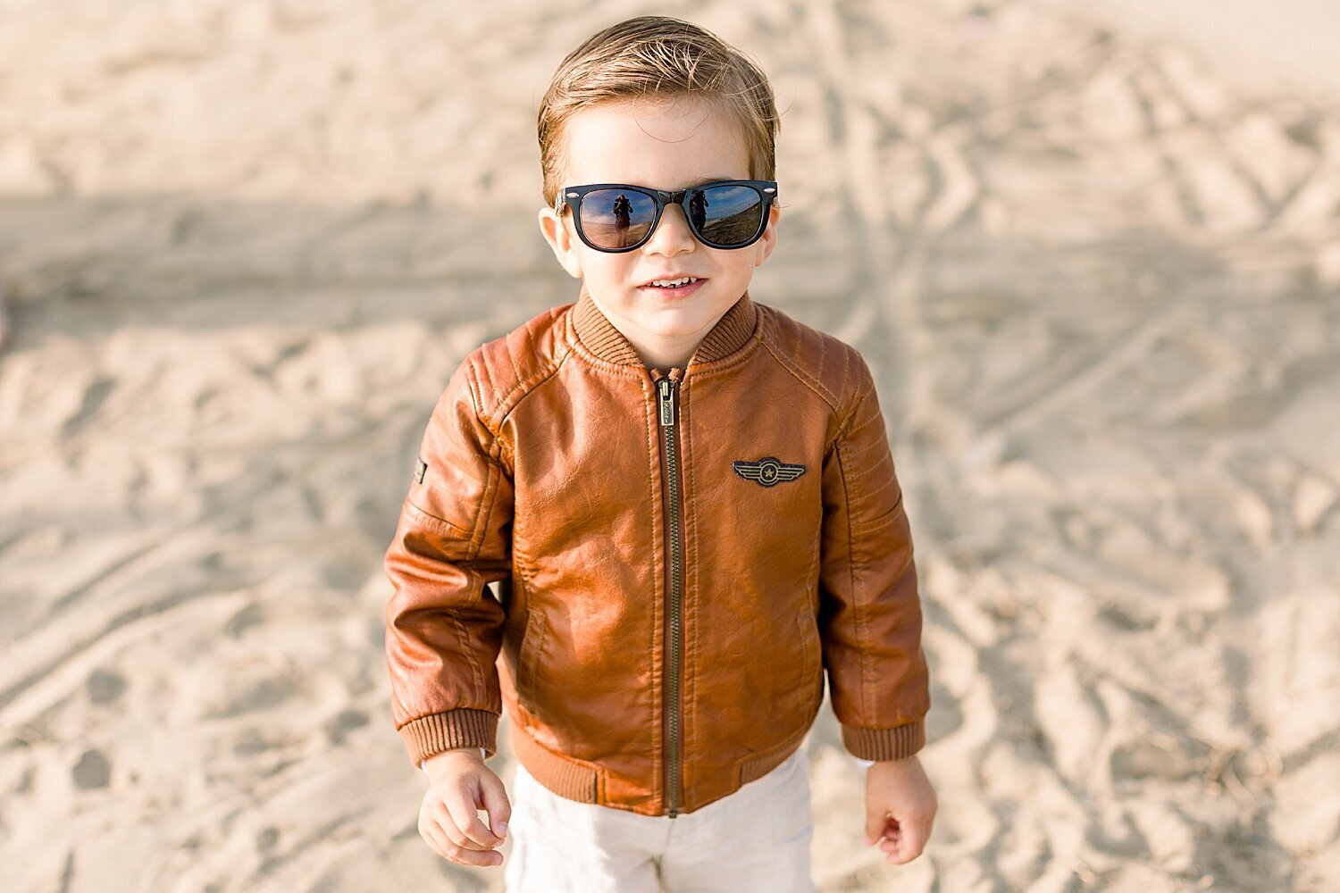 Photo of little boy in his leather jacket and sunglasses at the beach. Photos by Ambre Williams Photography. 