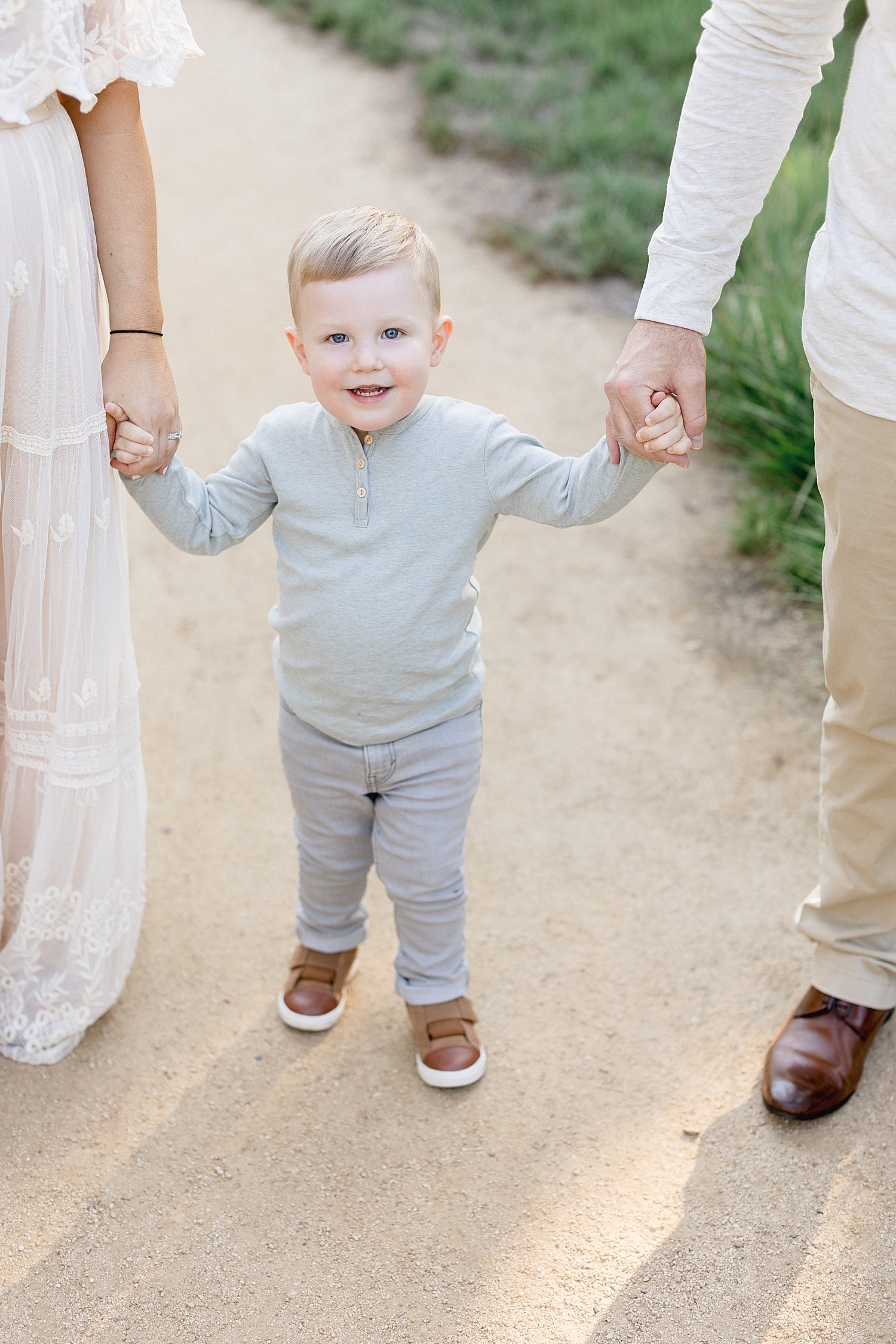 Child smiling and holding Mom and Dad's hands. Photo by Ambre Williams Photography.