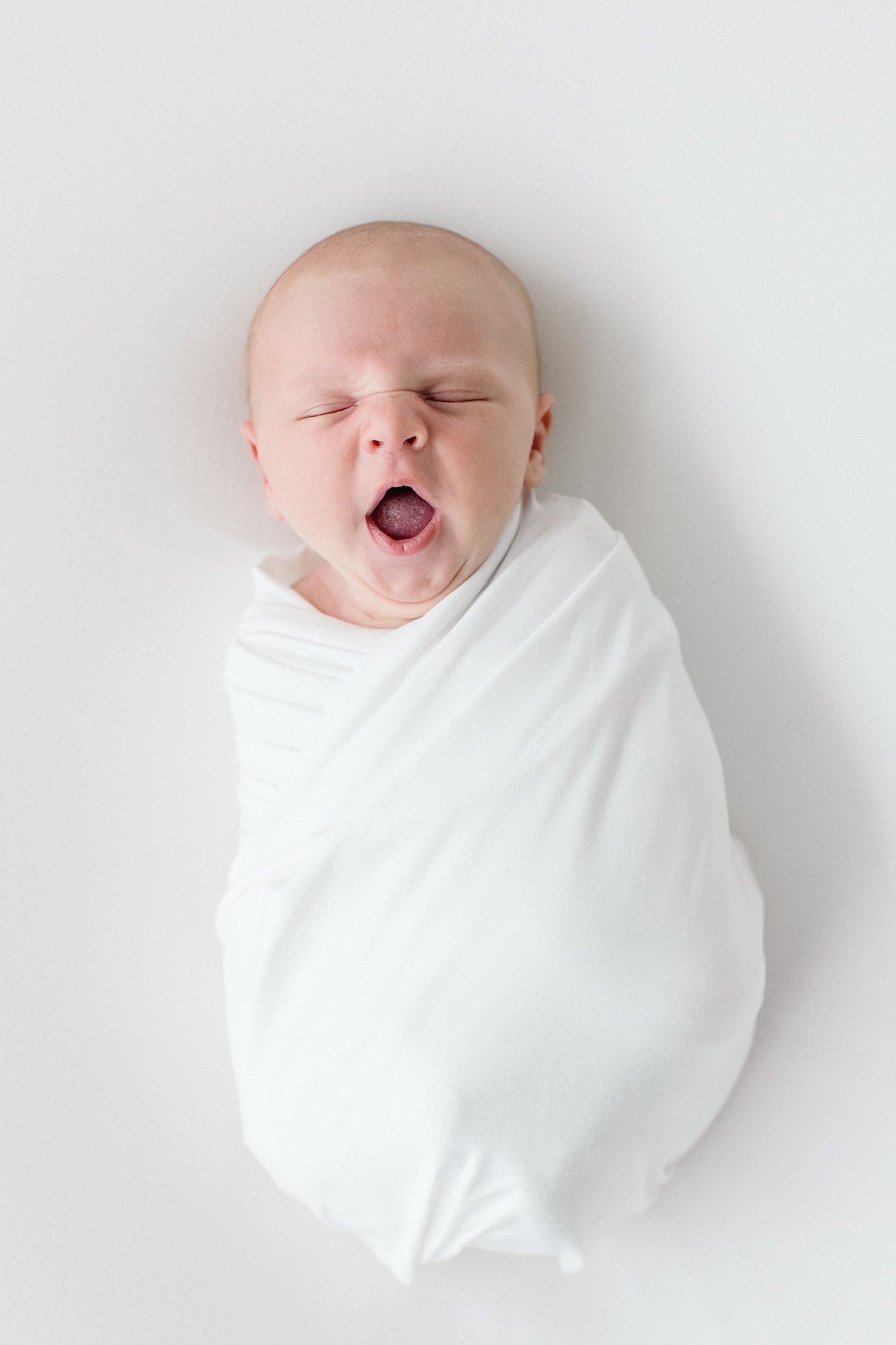 Baby yawns swaddled in white | Ambre Williams Photography
