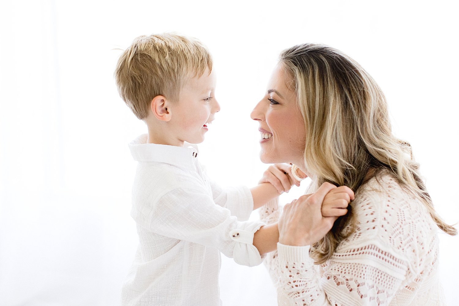 Mom smiles with son with white background in Newport Beach Studio with Ambre Williams Photography.