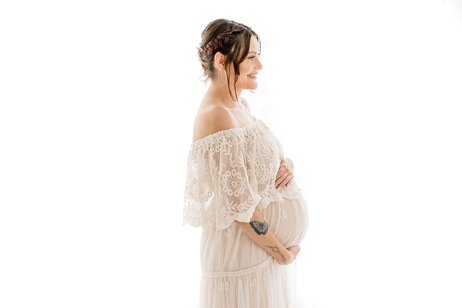 Smiling pregnant mother in long sheer white dress holding her belly for maternity session in Newport Beach with photographer Ambre Williams