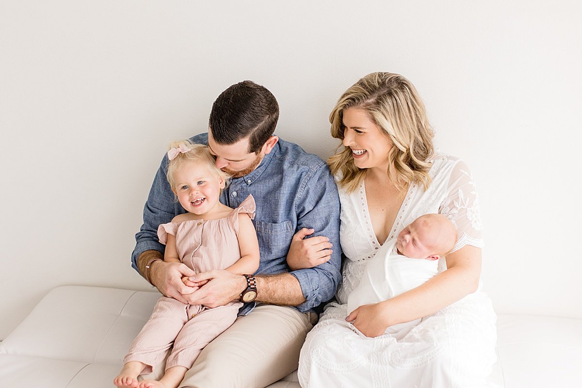 Dad kissing Big Sister and Mom holding Newborn in family studio session with Ambre Williams in Newport Beach