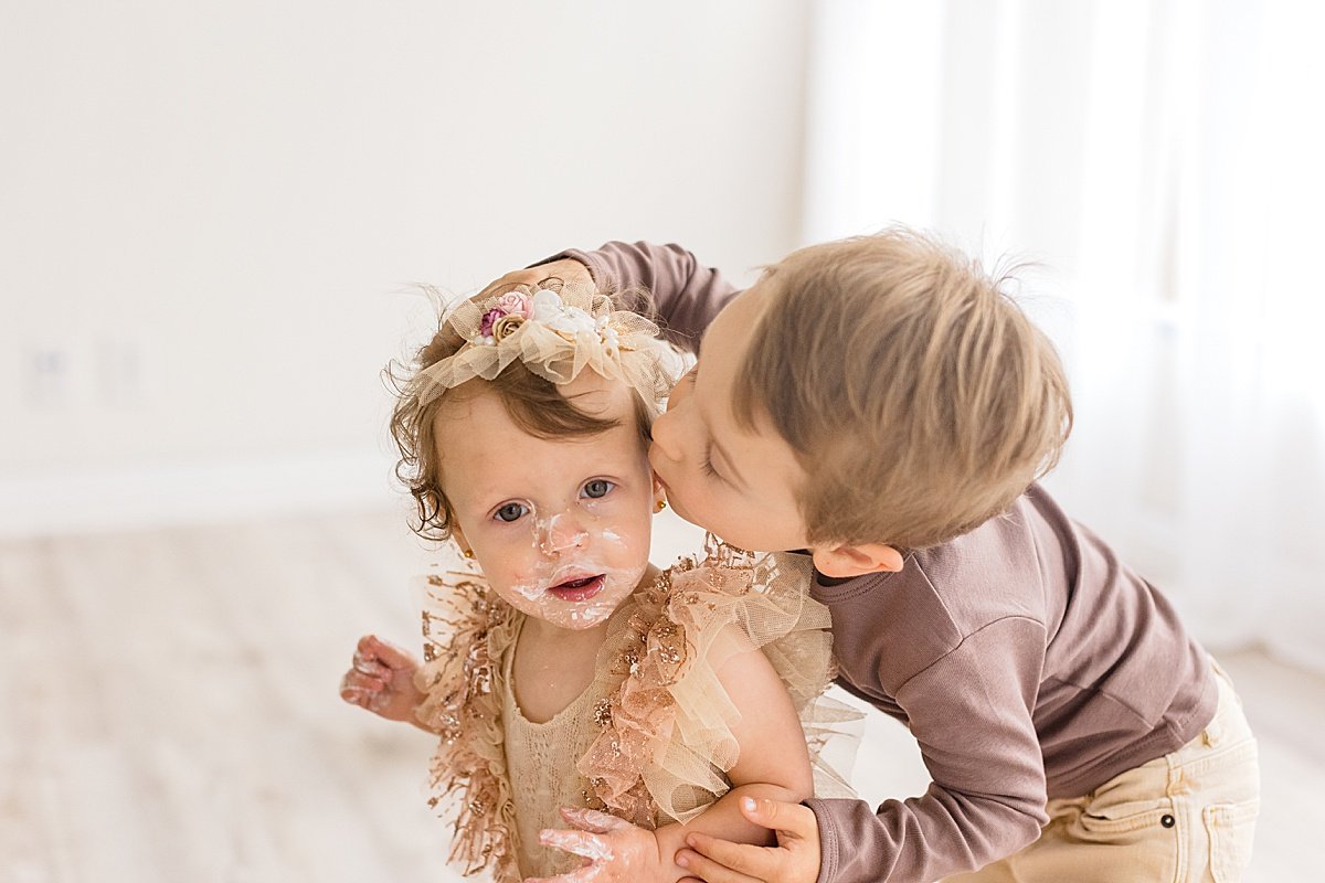 One Year Milestone candid portrait with big brother kissing little sister  | Ambre WIlliams Photography in Newport Beach Studio