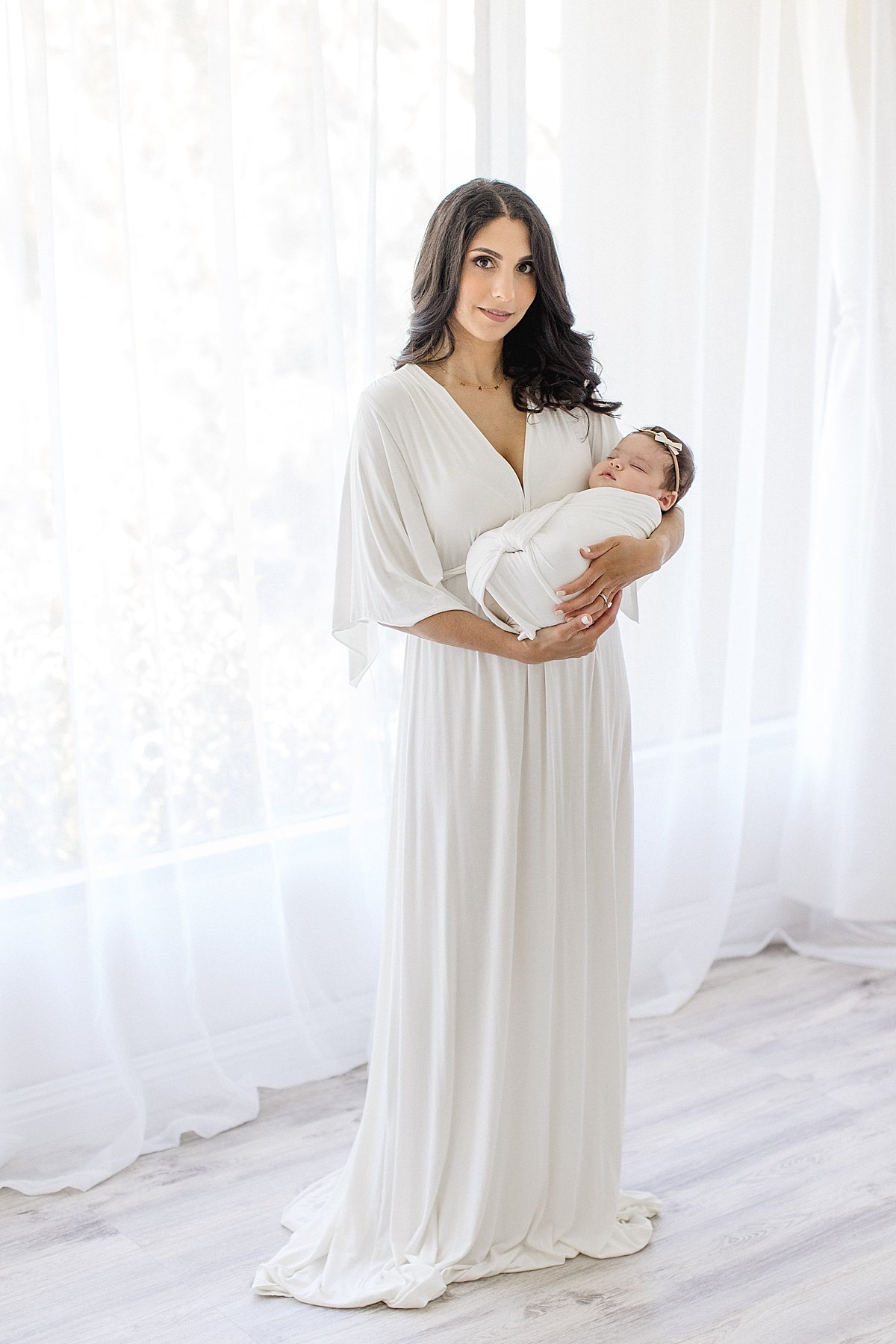 Beautiful mom wearing white dress holding newborn daughter | Ambre Williams Photography in Newport Beach Studio