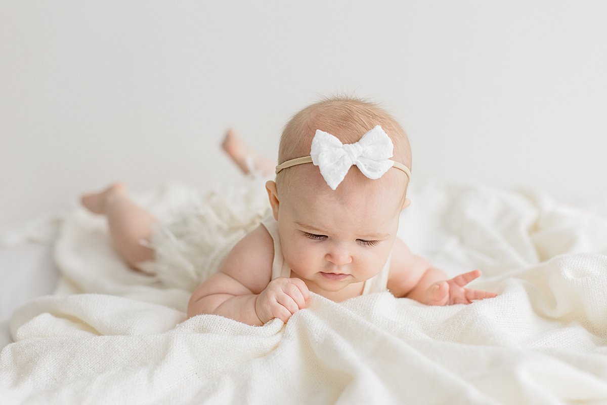 Happy baby girl wearing bow looking at white blanket | Ambre Williams Photography in Newport Beach